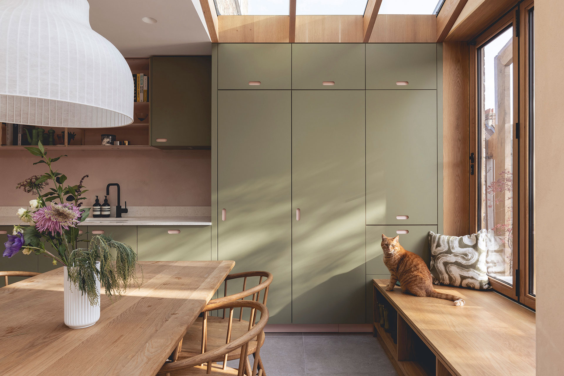Pink and green open plan Pluck kitchen including an island and plaster walls.