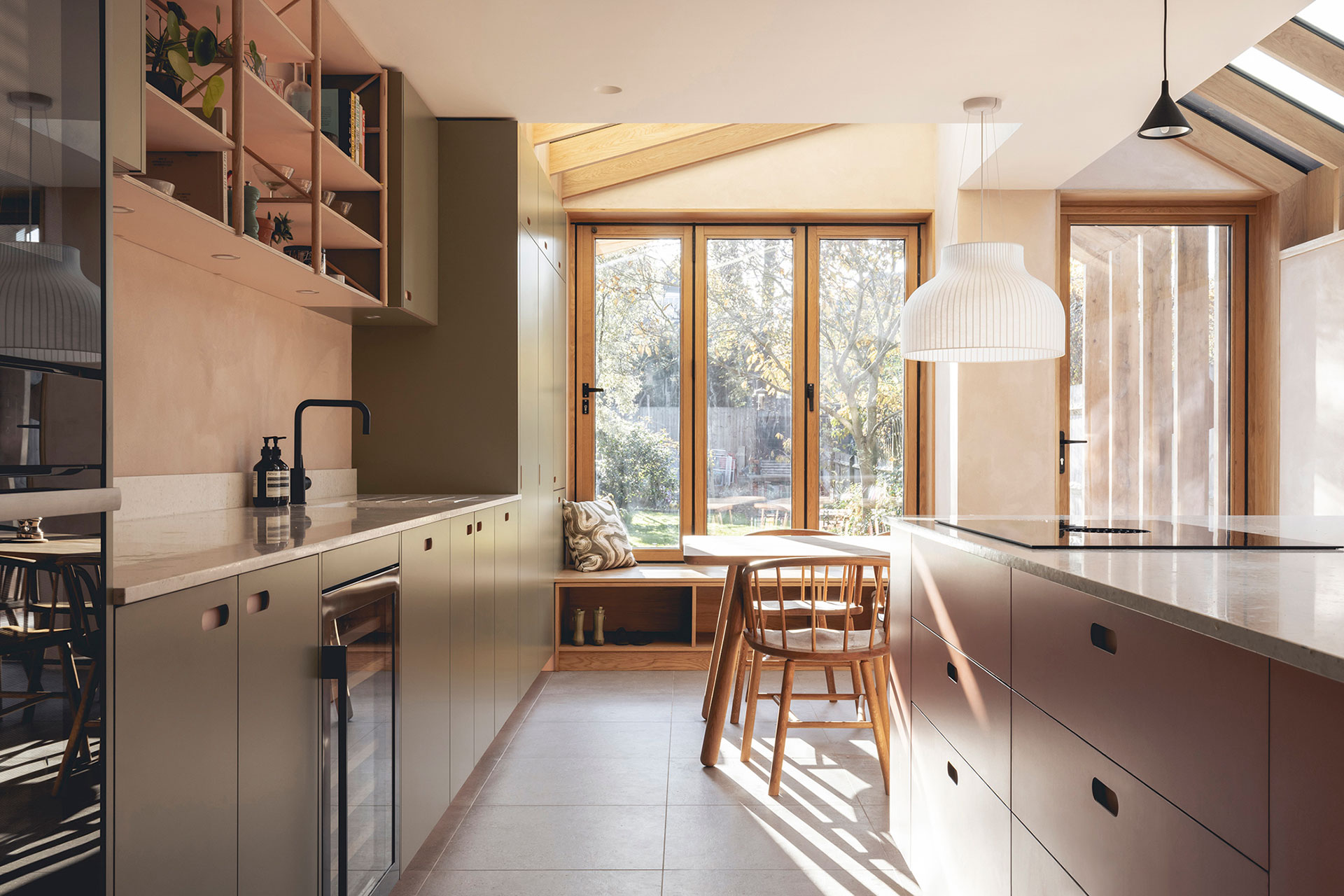 Pink and green open plan Pluck kitchen including an island and plaster walls.