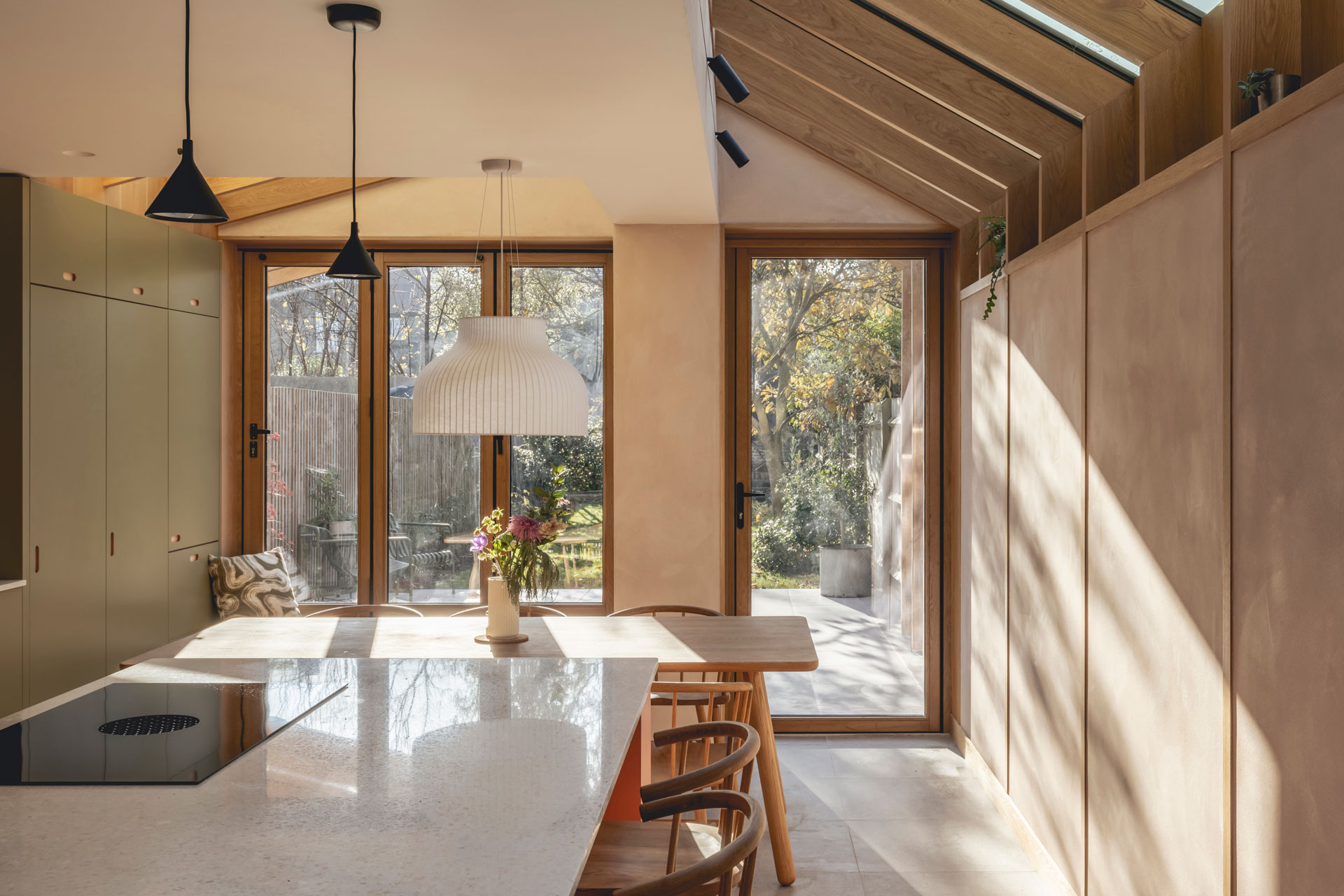Pink and green open plan Pluck kitchen including an island and plaster walls.