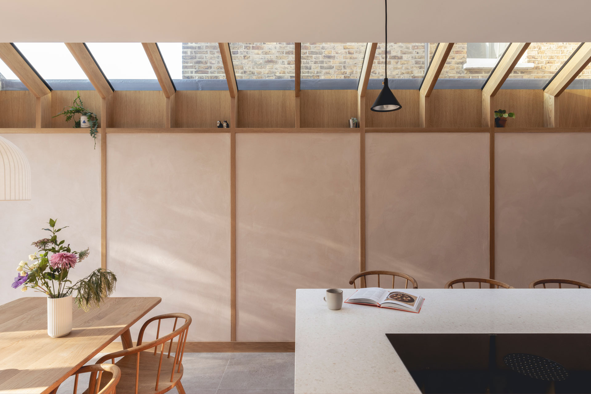 Pink and green open plan Pluck kitchen including an island and plaster walls.