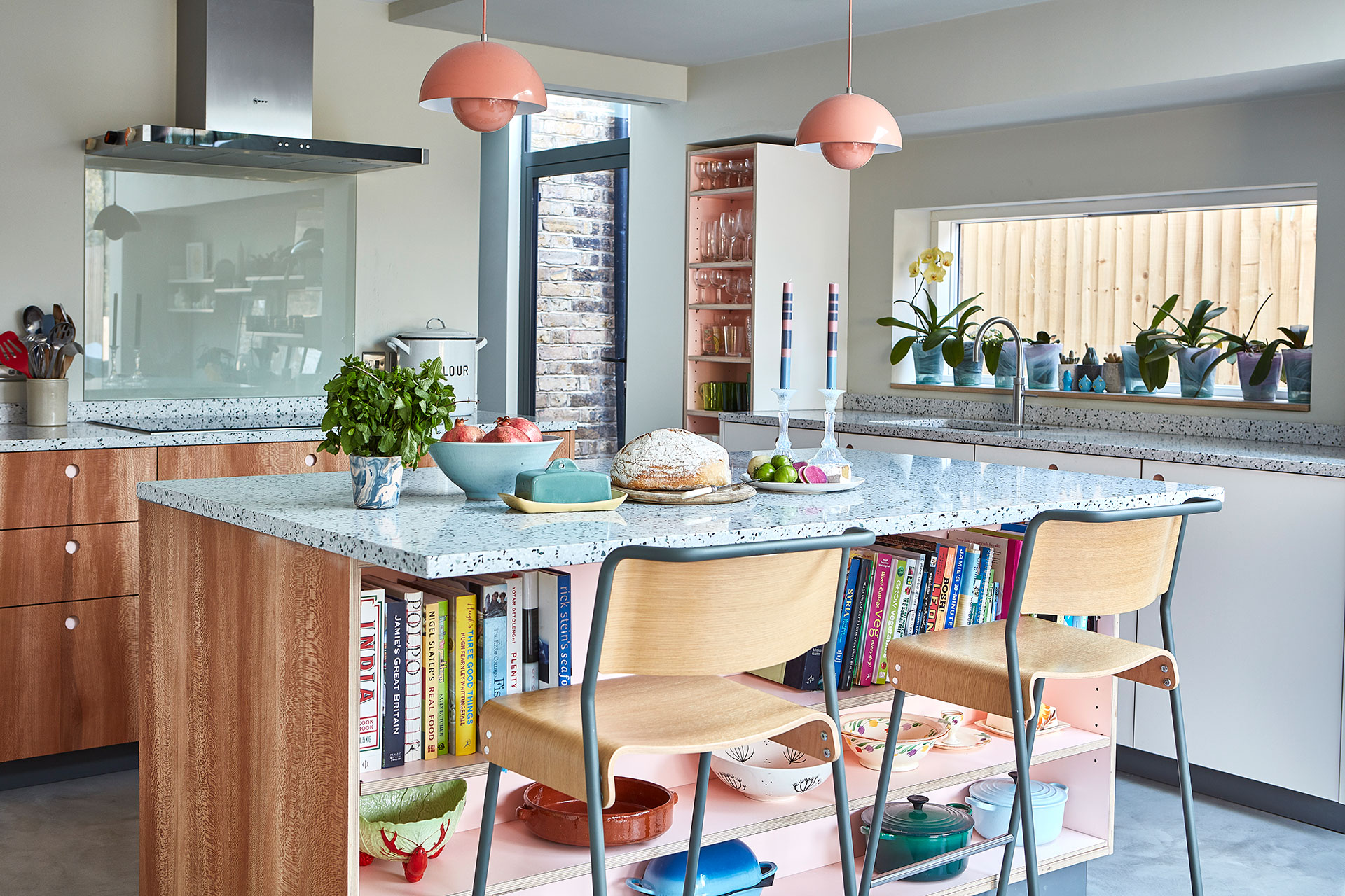 Open plan pink, white and London Plane wood Pluck kitchen including an island and terrazzo countertop.