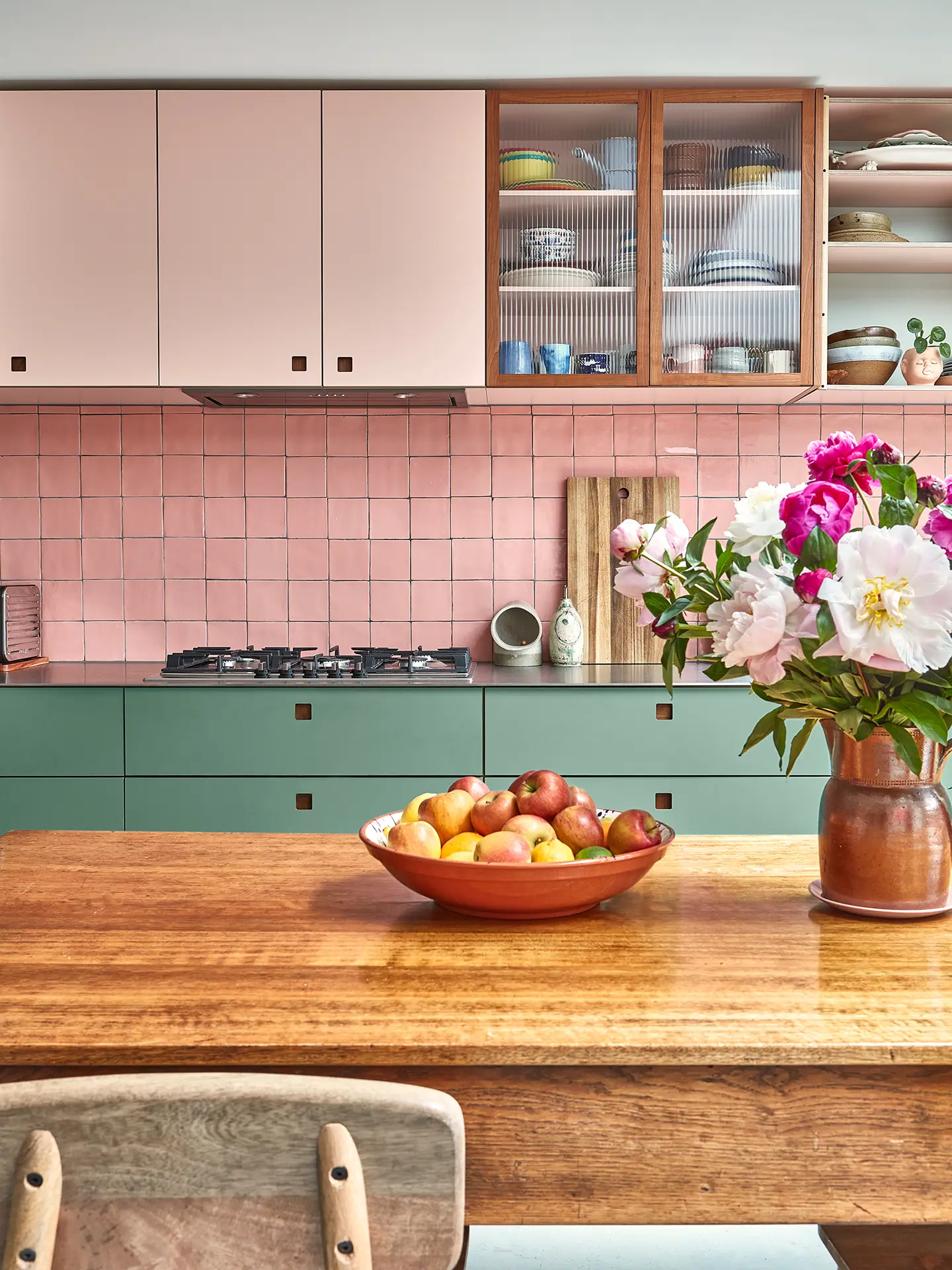 Sleek stainless steel topped pink and green cabinetry with a wooden kitchen table.