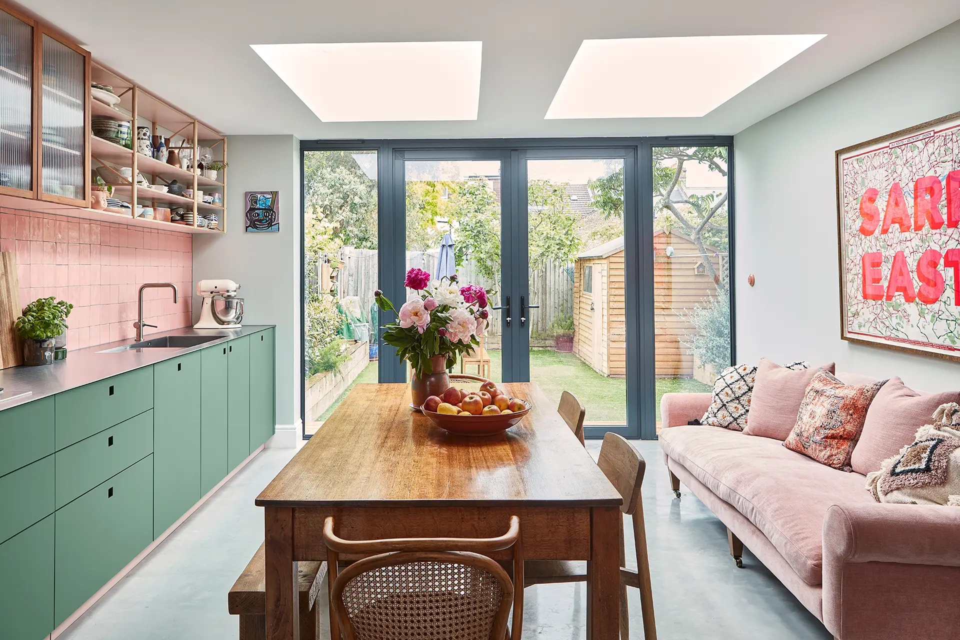 Pink and green Pluck kitchen cabinetry including a multi-coloured larder with sleek stainless steel worktops and glossy tiles.
