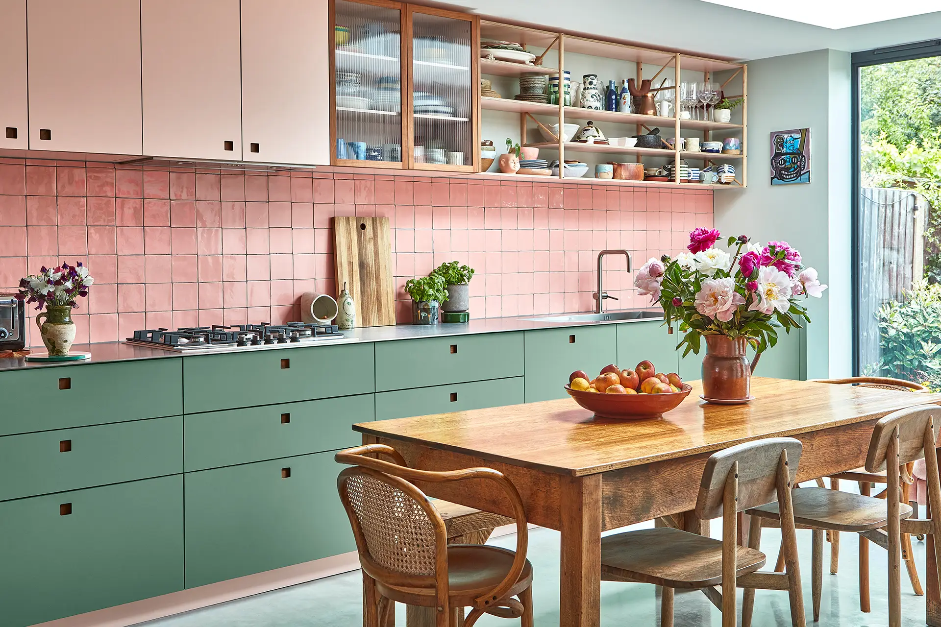 Pink and green Pluck kitchen cabinetry including a multi-coloured larder with sleek stainless steel worktops and glossy tiles.