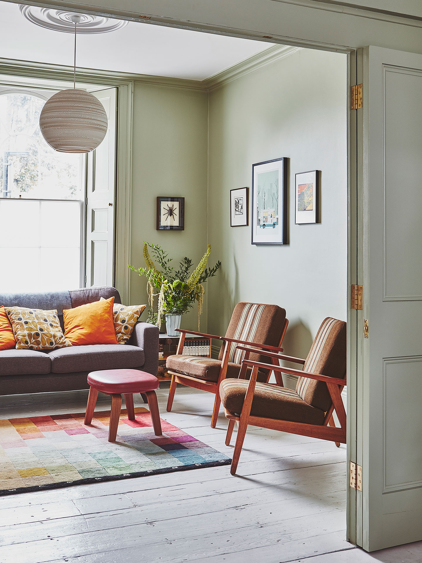 Sofa and arm chairs in a light green living room with a colourful rug.
