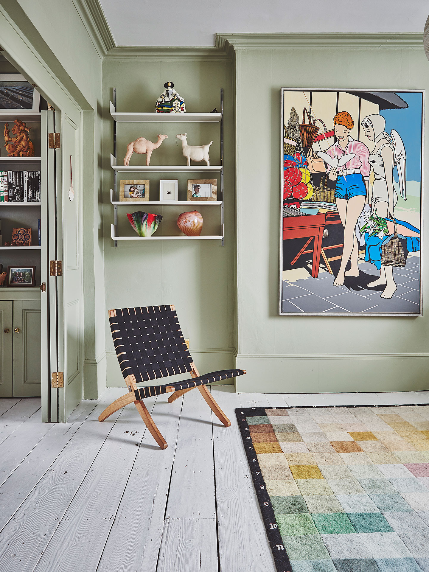 Sitting room with pale green walls, wooden flooring, colour swatch rug, artwork and a chair.