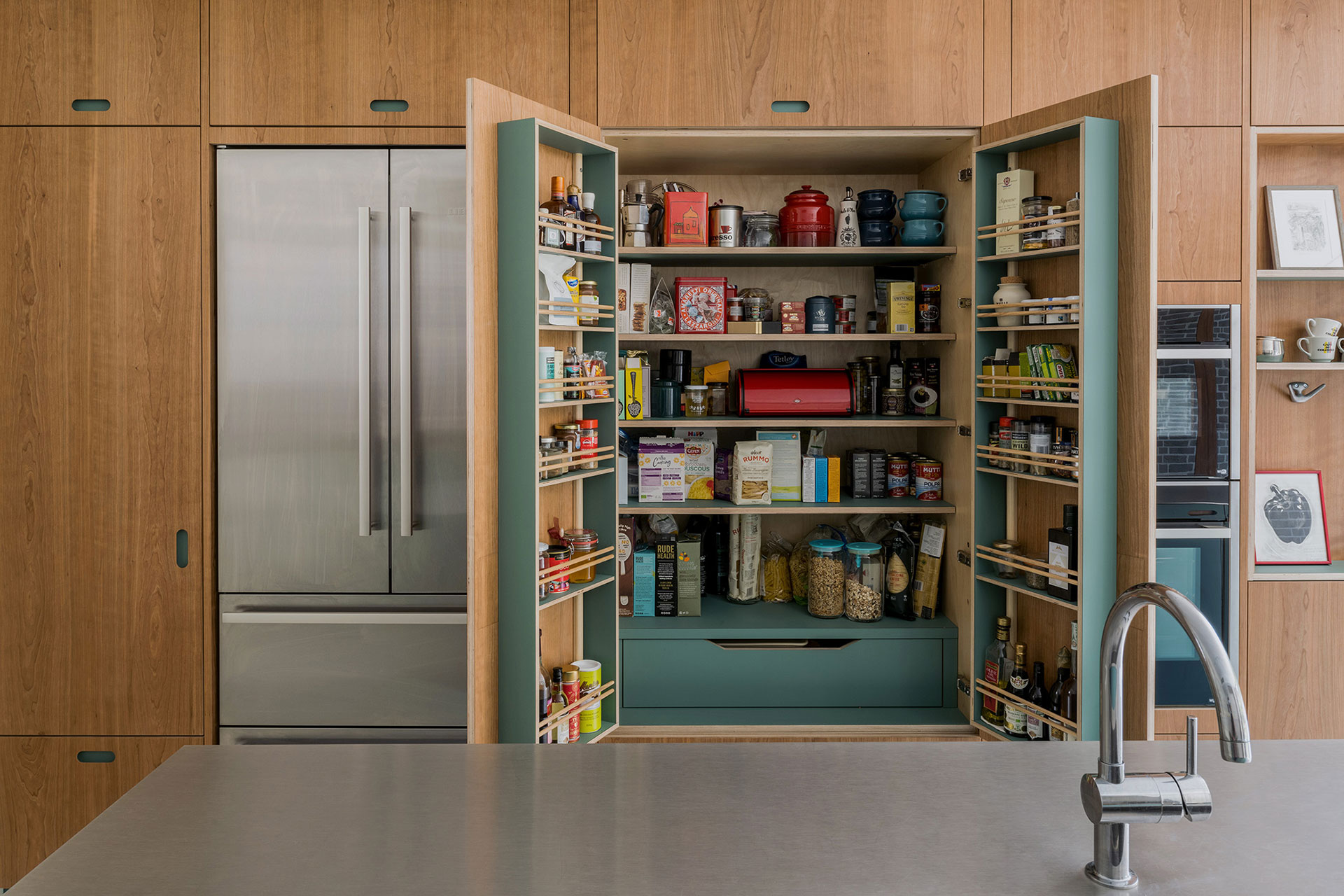 Warm Cherry wood and matt green kitchen cabinetry with sleek stainless steel worktops and white tiles.