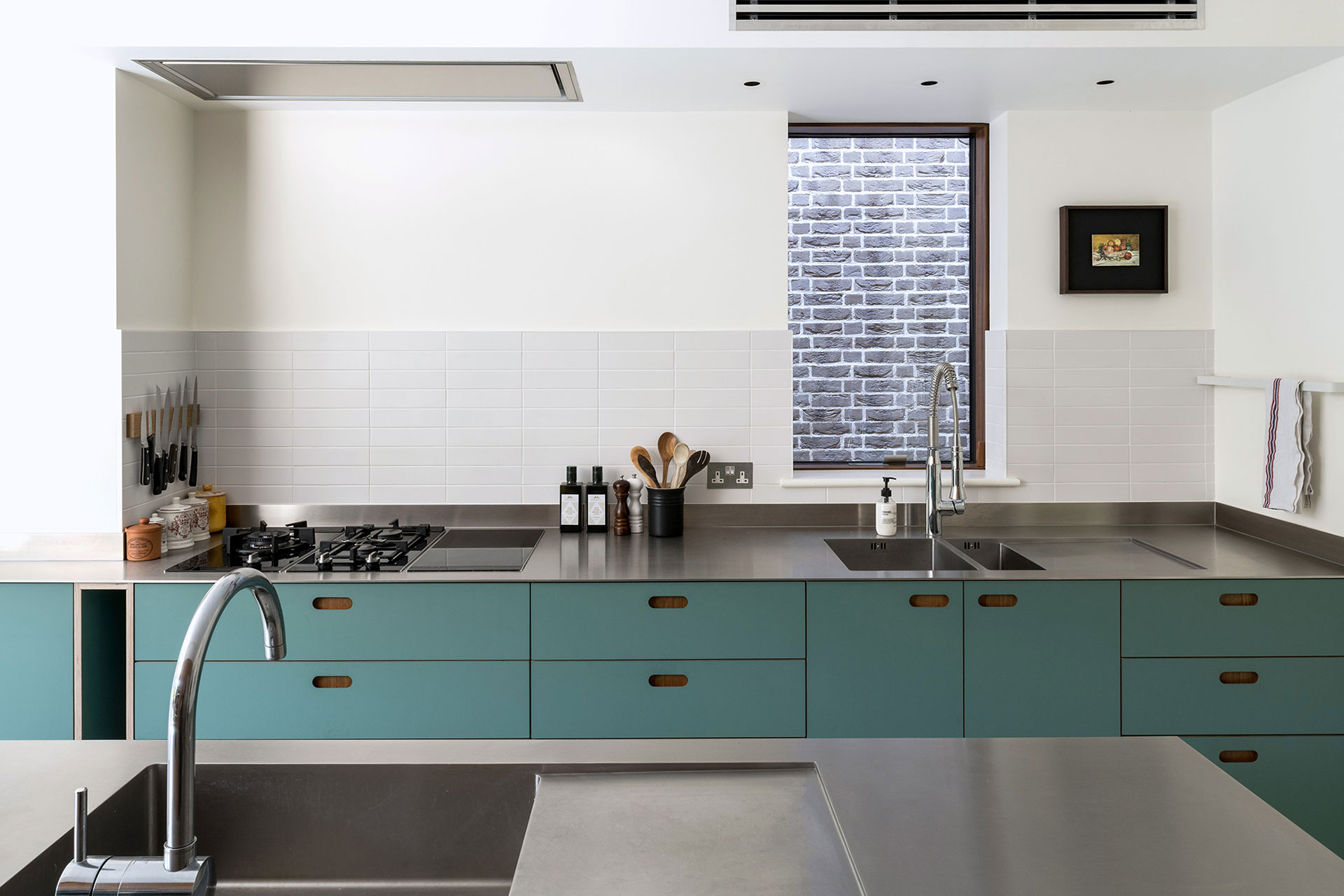 Warm Cherry wood and matt green kitchen cabinetry with sleek stainless steel worktops and white tiles.