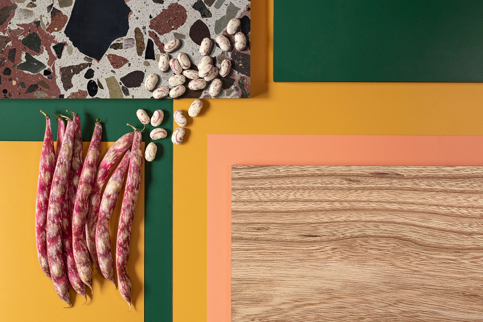 Colourful kitchen palette of bottle green, coral pink, mustard yellow, textured Elm wood and terrazzo with borlotti beans.