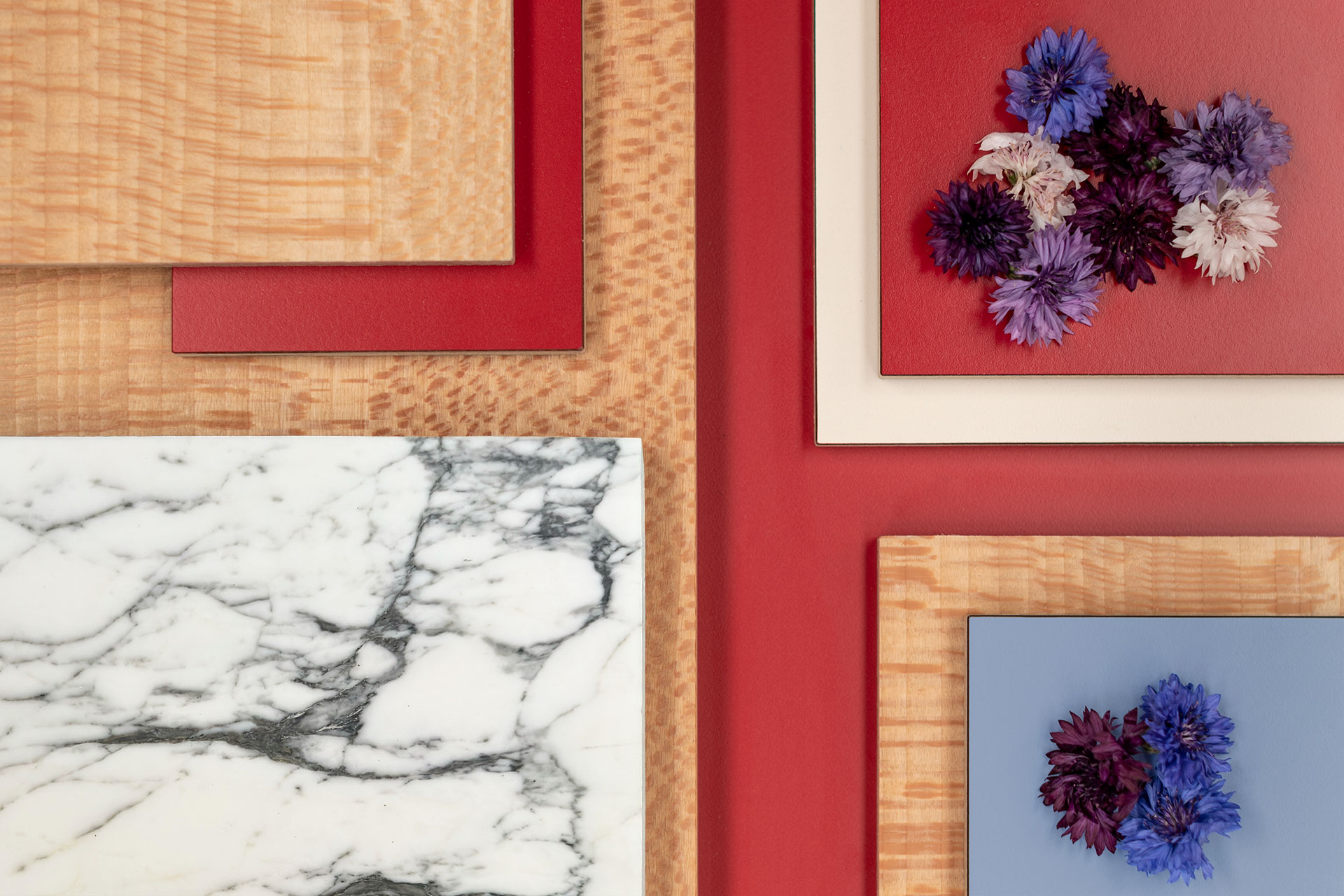 Vibrant red, pale blue, beige and London Plane wood grain kitchen inspiration with natural stone and scattered flowers.