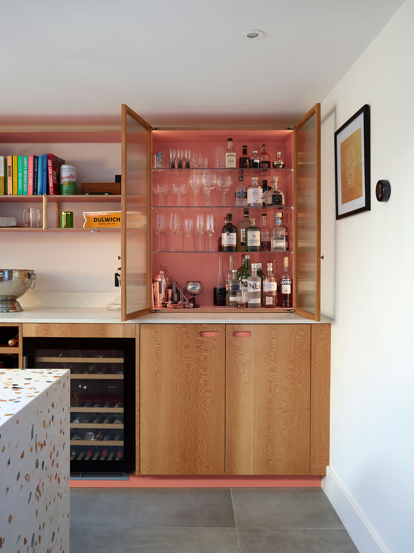 A fluted glass cocktail cabinet in an open plan dinner party kitchen with a terrazzo waterfall edge island.