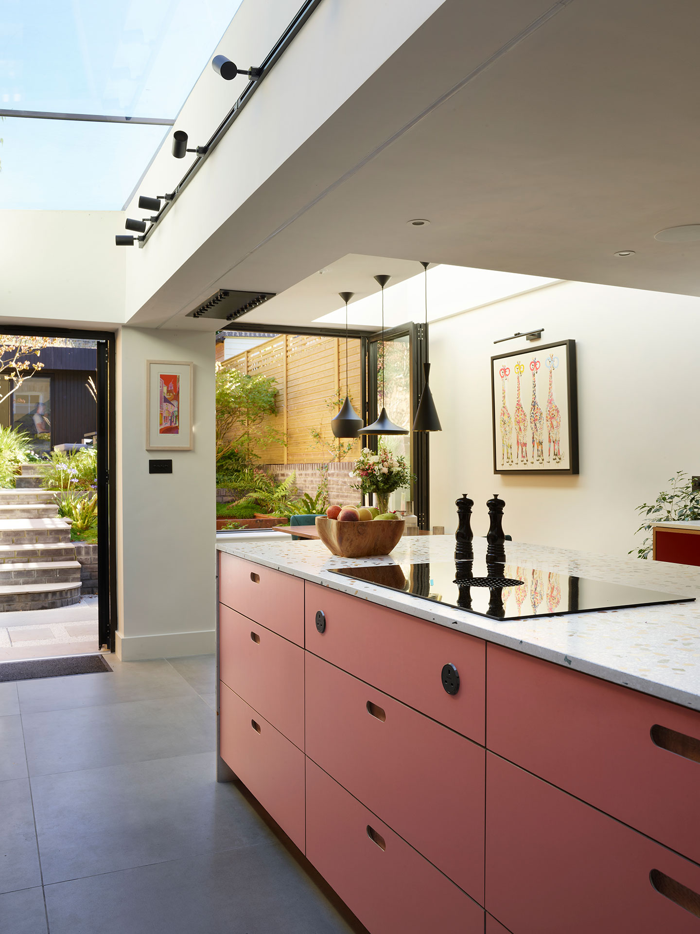 Dark grey and coral pink open plan kitchen with a London Plane wood cocktail cabinet and waterfall edge terrazzo topped island.
