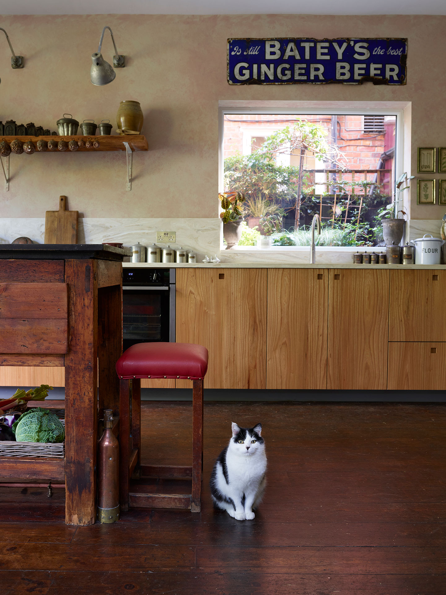 Moody kitchen including Elm wood and khaki cabinetry in an open plan space with a vintage typesetting table island and antiques.