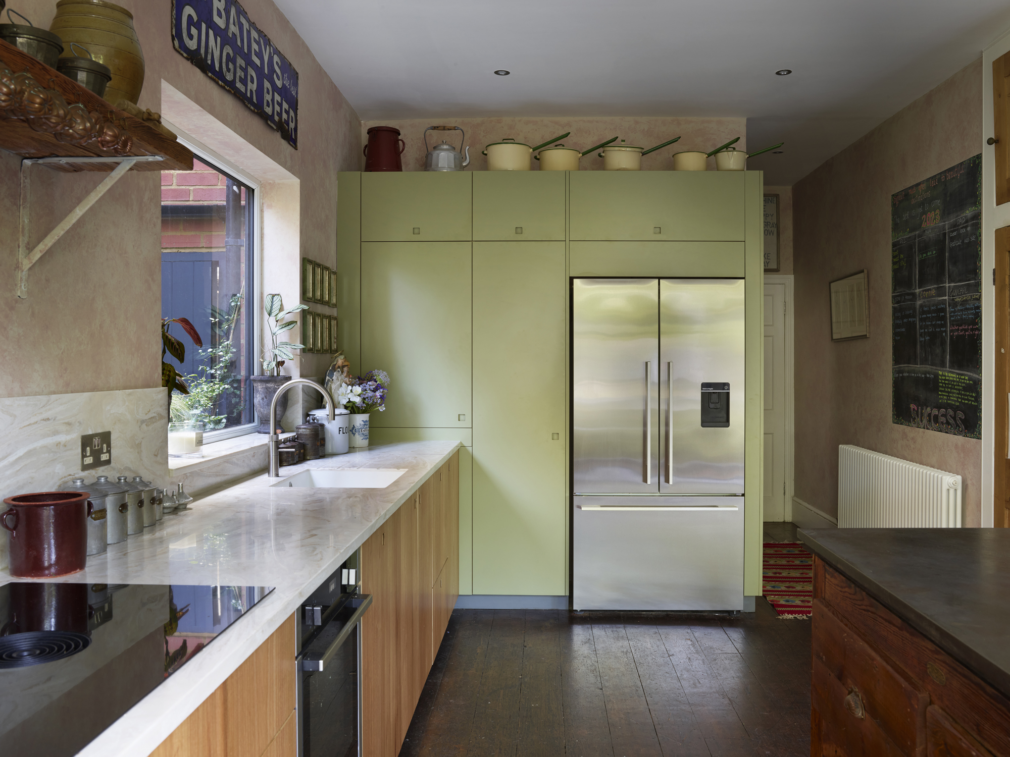 Moody kitchen including Elm wood and khaki cabinetry in an open plan space with a vintage typesetting table island and antiques.