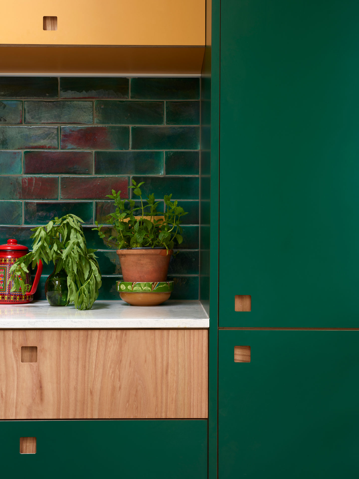 Colourful Pluck kitchen with green, yellow and wood cabinets and glossy tiles home to an artist.
