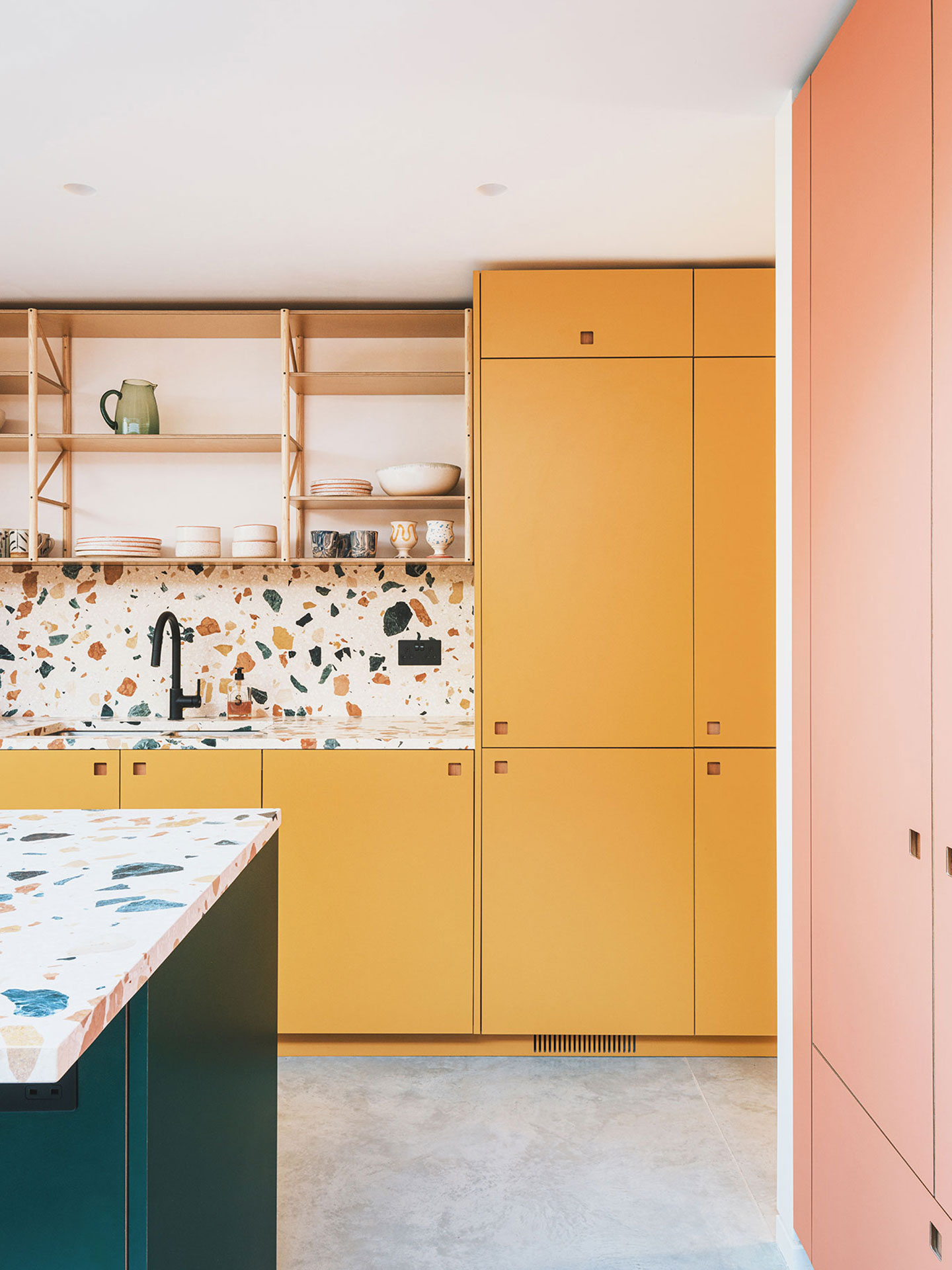 Colourful open plan kitchen with three bold Pluck hues, a Brixton dresser on an exposed brick wall and terrazzo worktops.