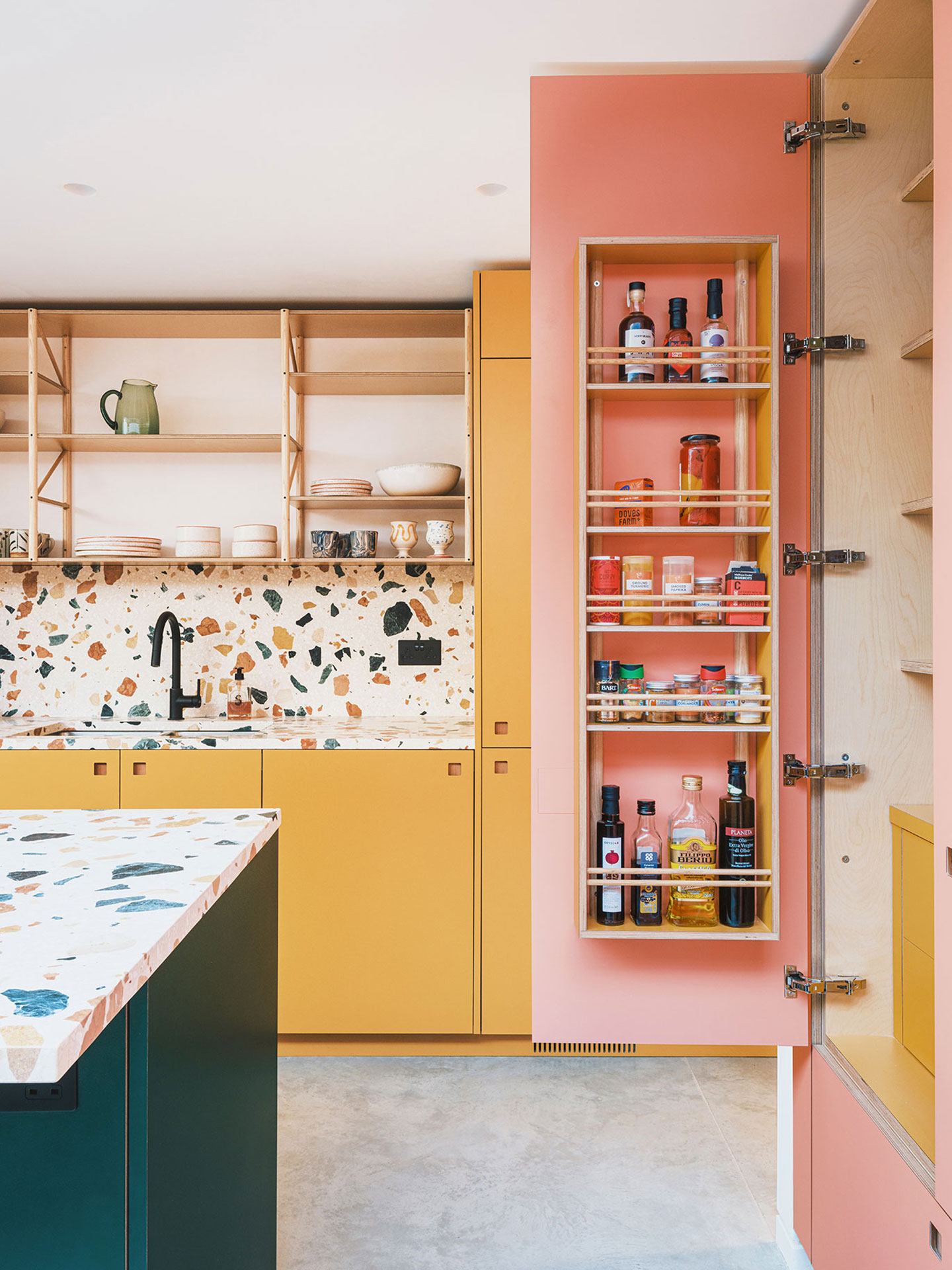 Colourful kitchen with a terrazzo topped island, shelving, dresser and banquette seating.