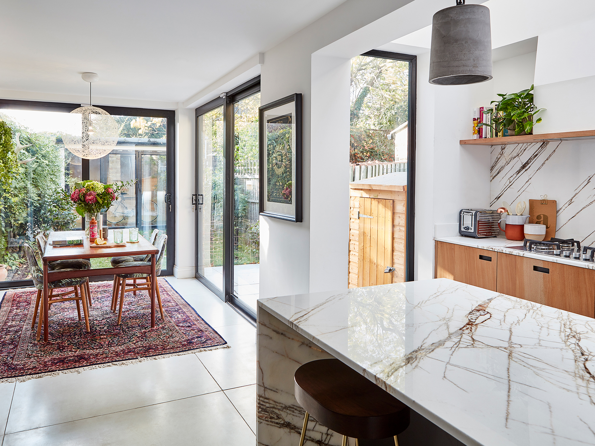 Cosy dining area of an open plan kitchen with a vintage dining table and upholstered chairs on a red Persian rug.