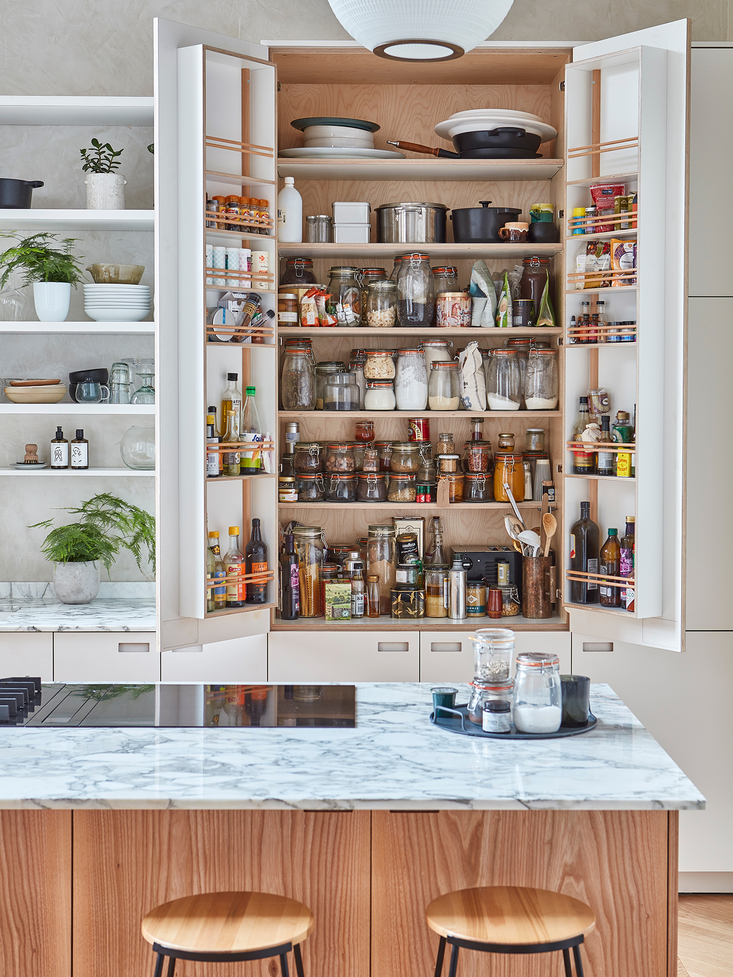 The doors of a tall white larder cupboard are open to reveal neatly arranged ingredients inside.