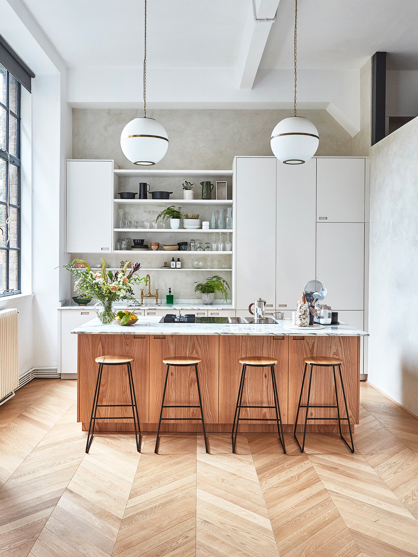 A kitchen set in a converted Victorian school with extra tall ceilings. The wall cabinets are white and the island is wood.