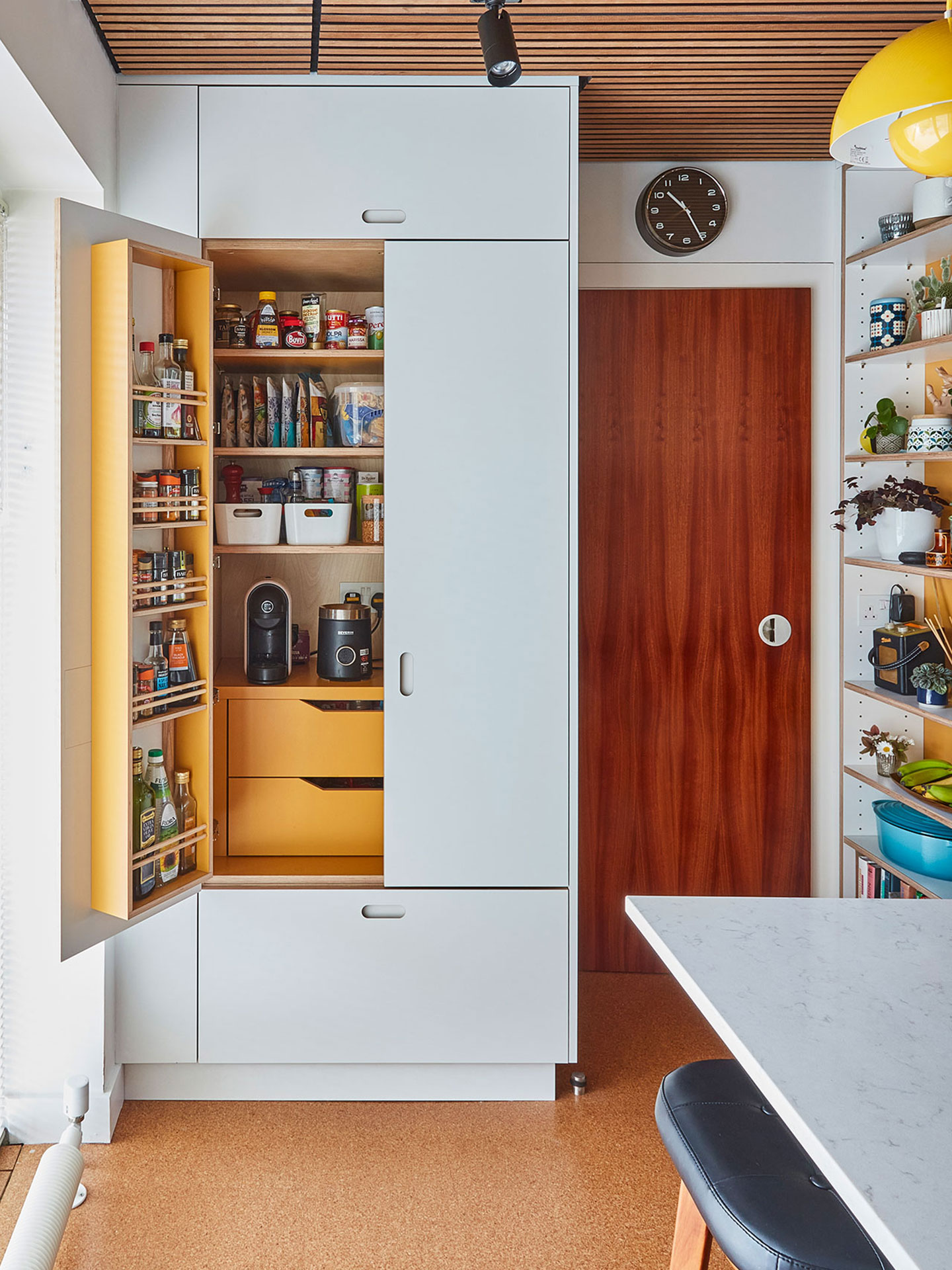Modernist white Pluck kitchen including a waterfall edge island and larder with glossy blue kit-kat tiles and cork flooring.