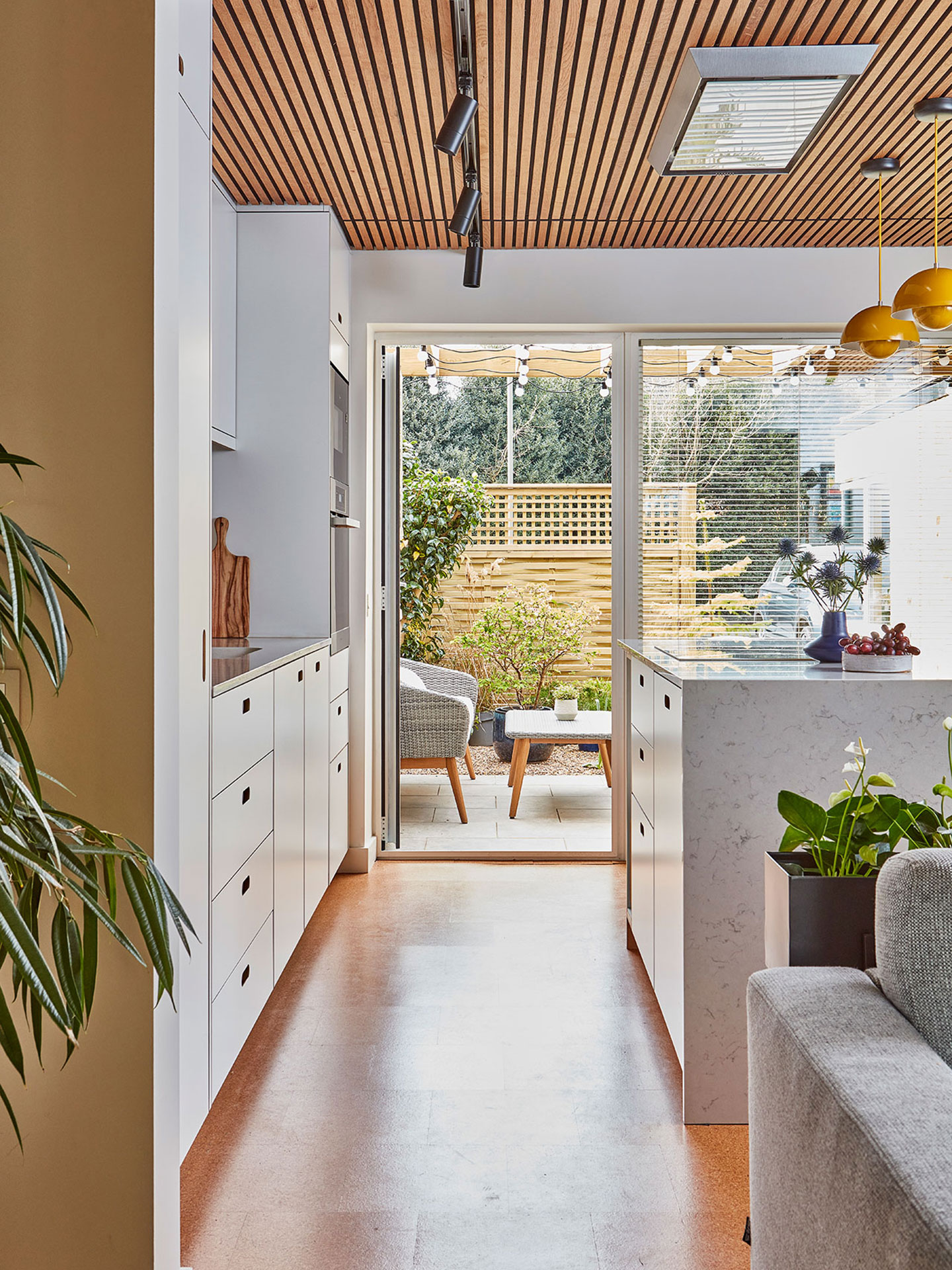Modernist white Pluck kitchen including a waterfall edge island and larder with glossy blue kit-kat tiles and cork flooring.