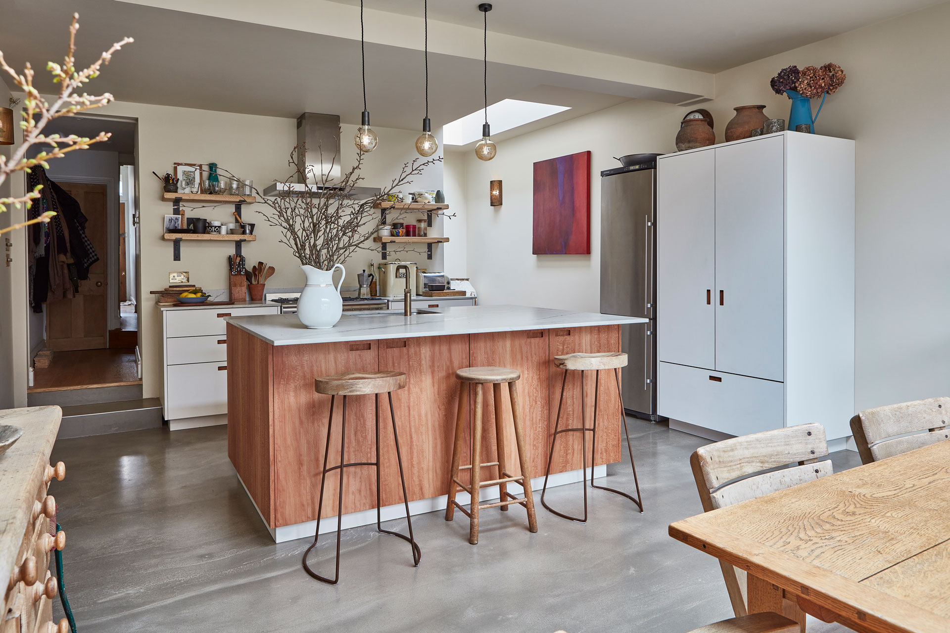 Open plan kitchen with neutral wood and white cabinetry topped with natural stone.