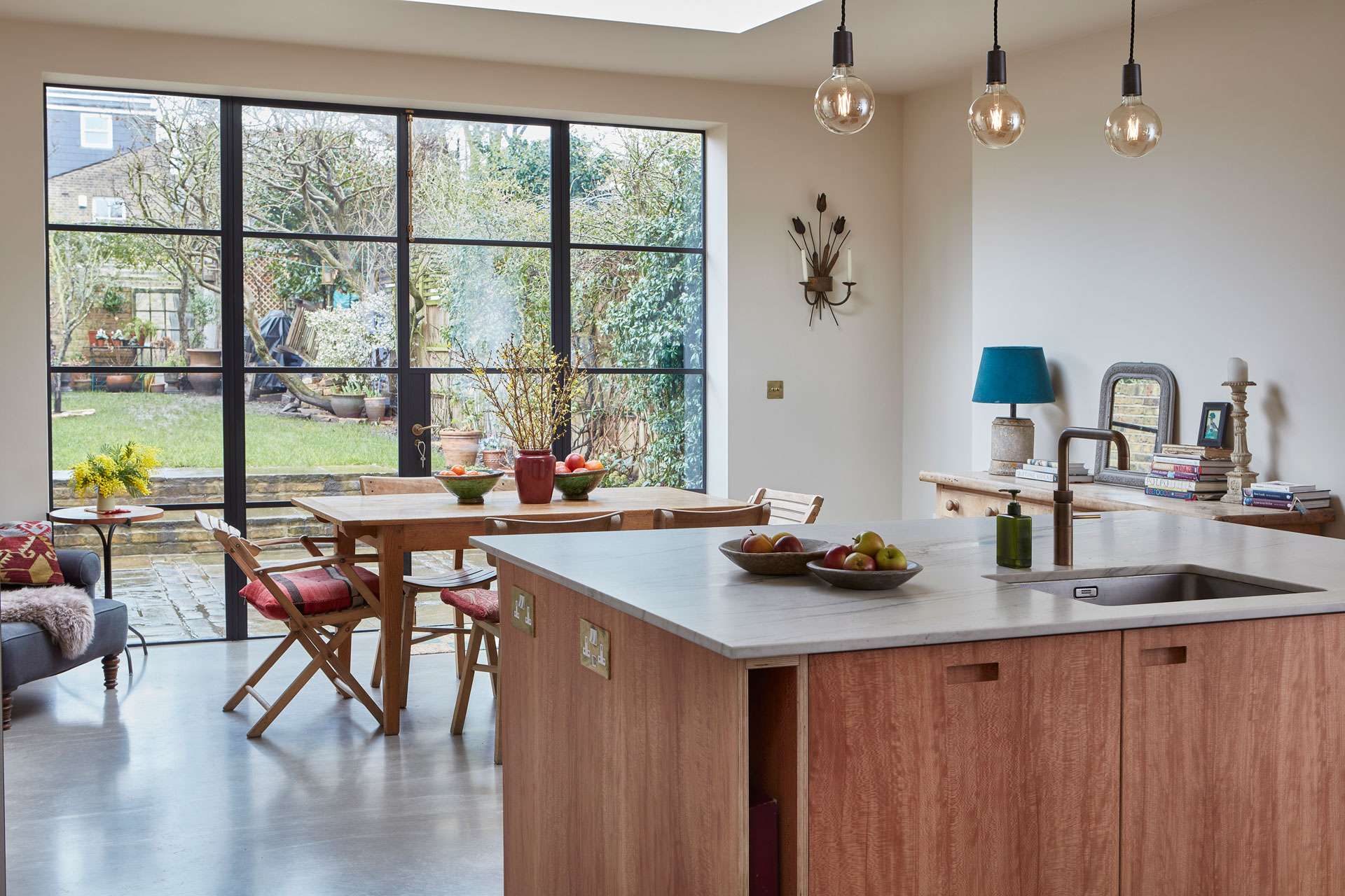 Open plan kitchen with neutral wood and white cabinetry topped with natural stone.