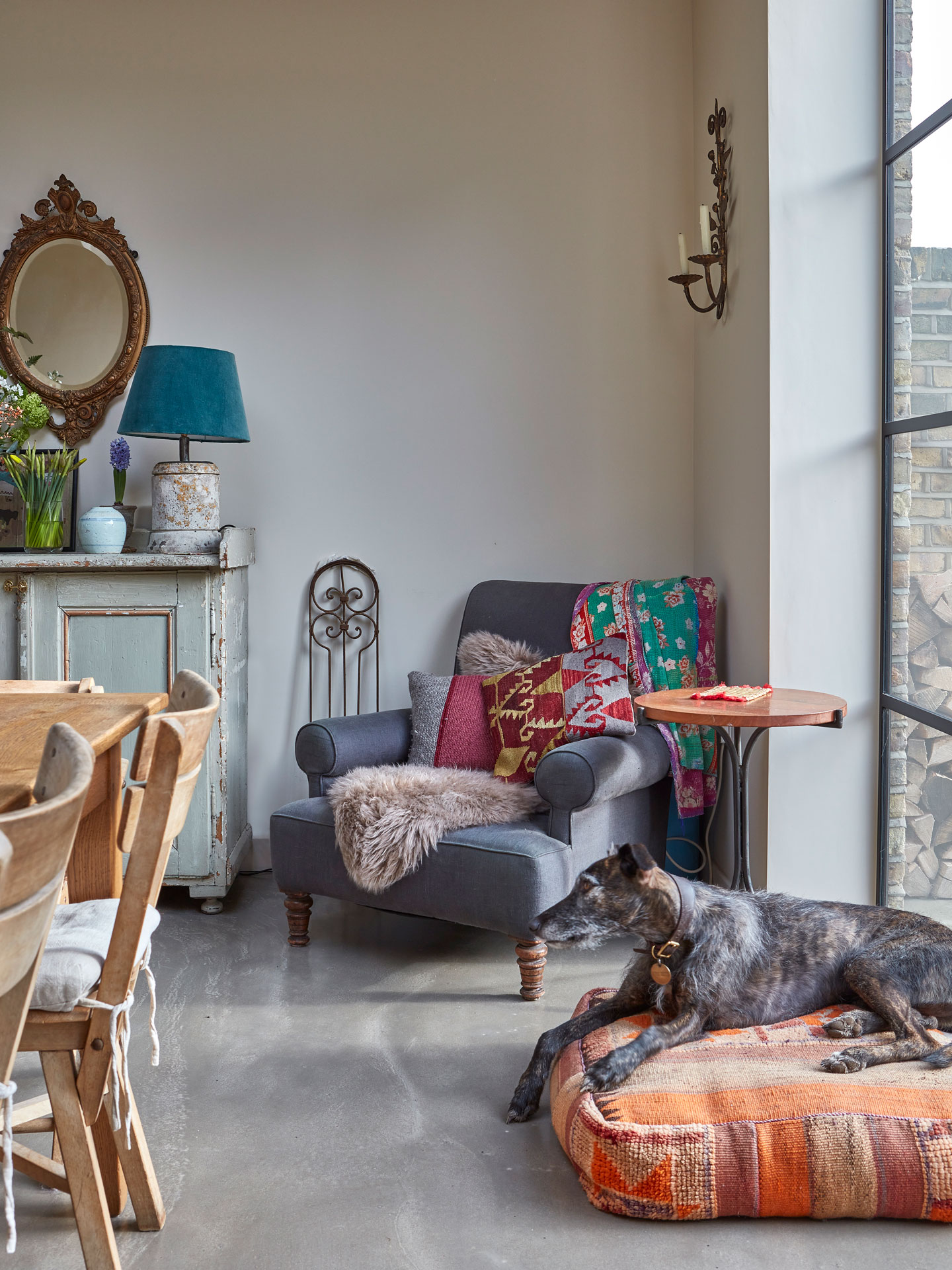 Cosy corner of an open plan kitchen with an armchair, antique furniture and a dog resting.