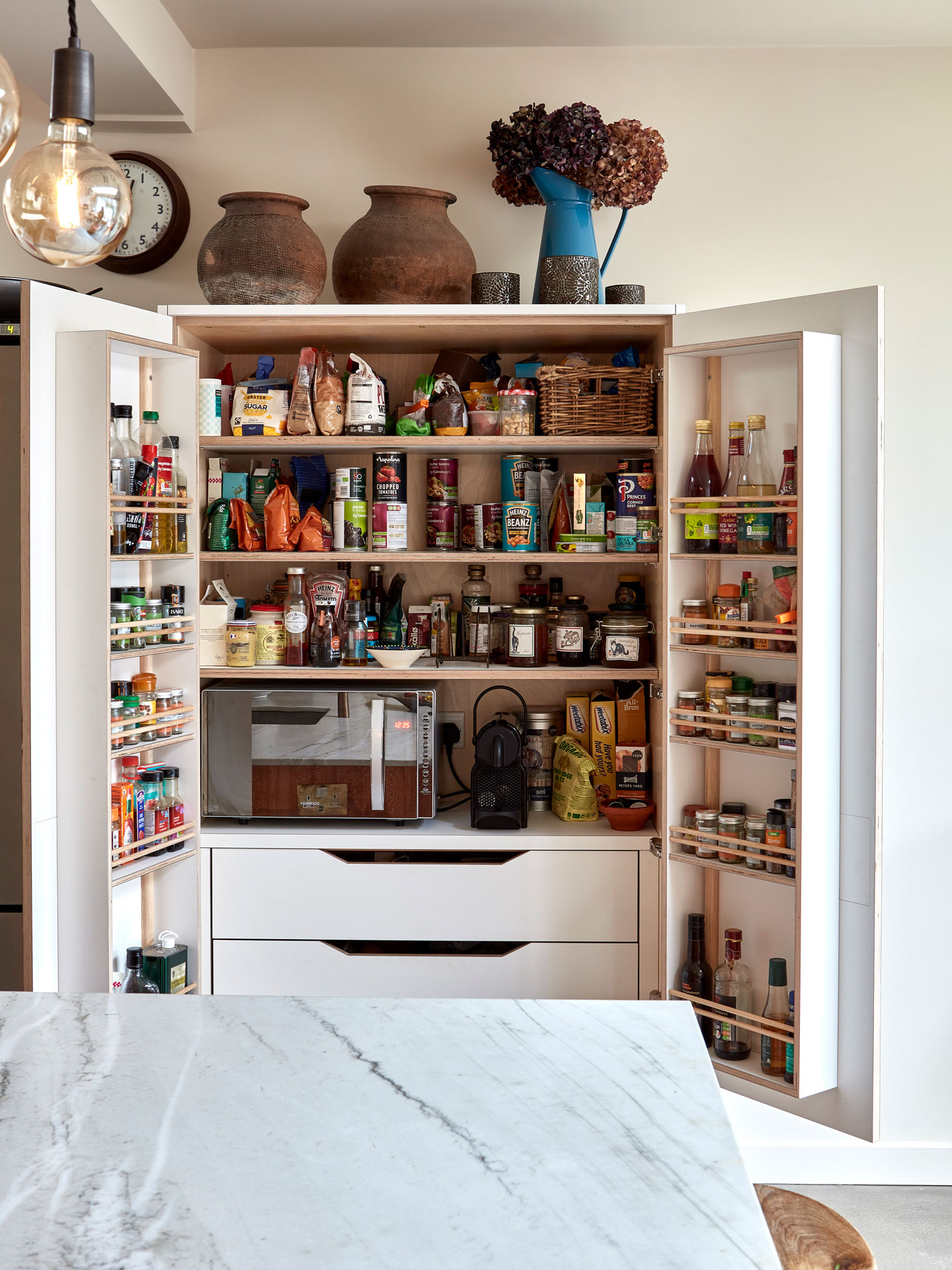 White larder cupboard with doors open revealing spice racks, ingredients and small appliances.