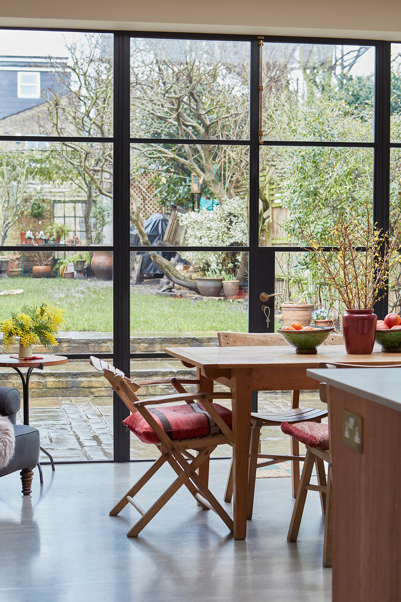 Open plan kitchen with wood cabinetry, a large antique dining table and crittall windows.