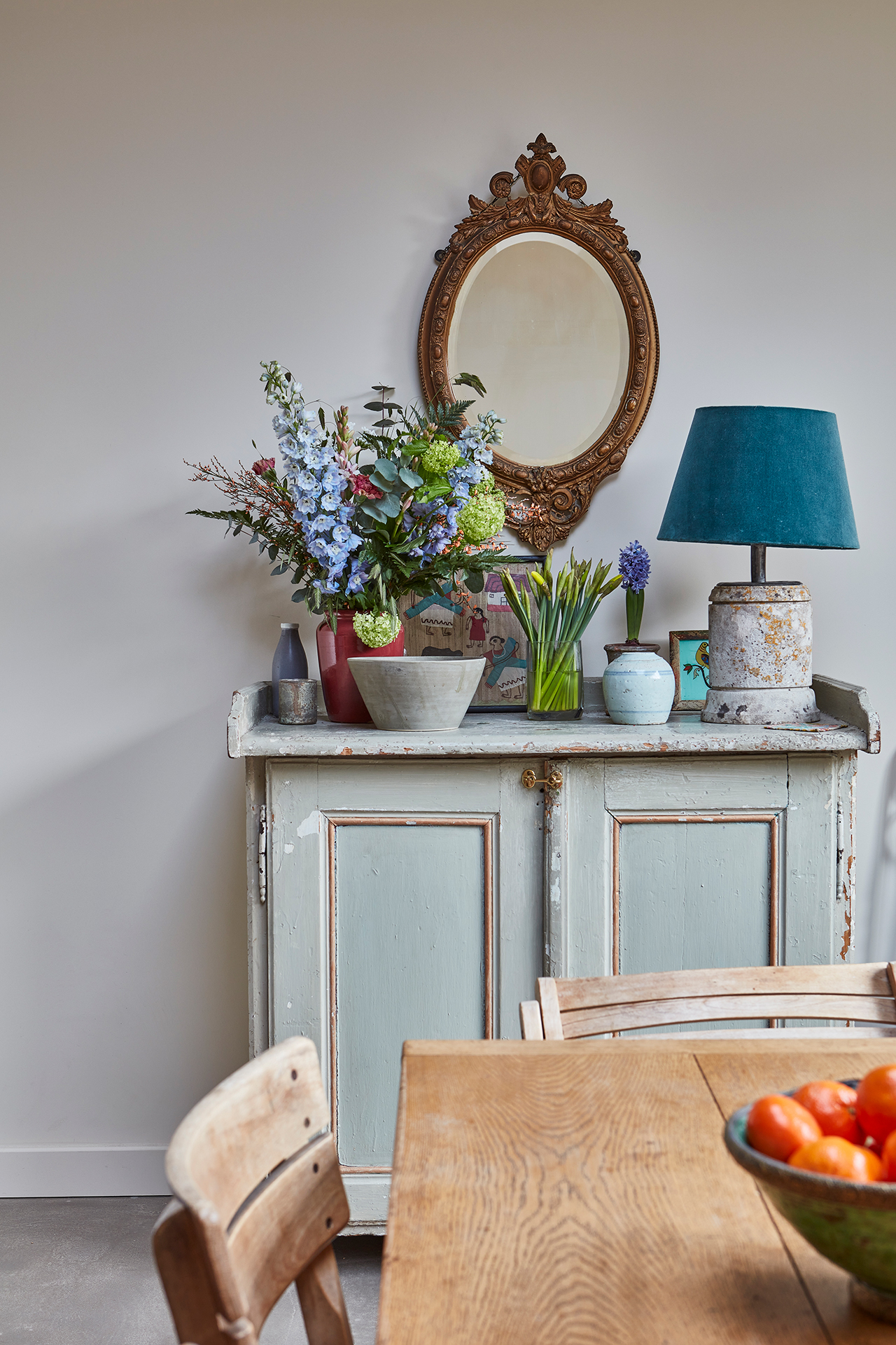 Painted Antique cupboard with fresh flowers and a ceramic lamp arranged on top.