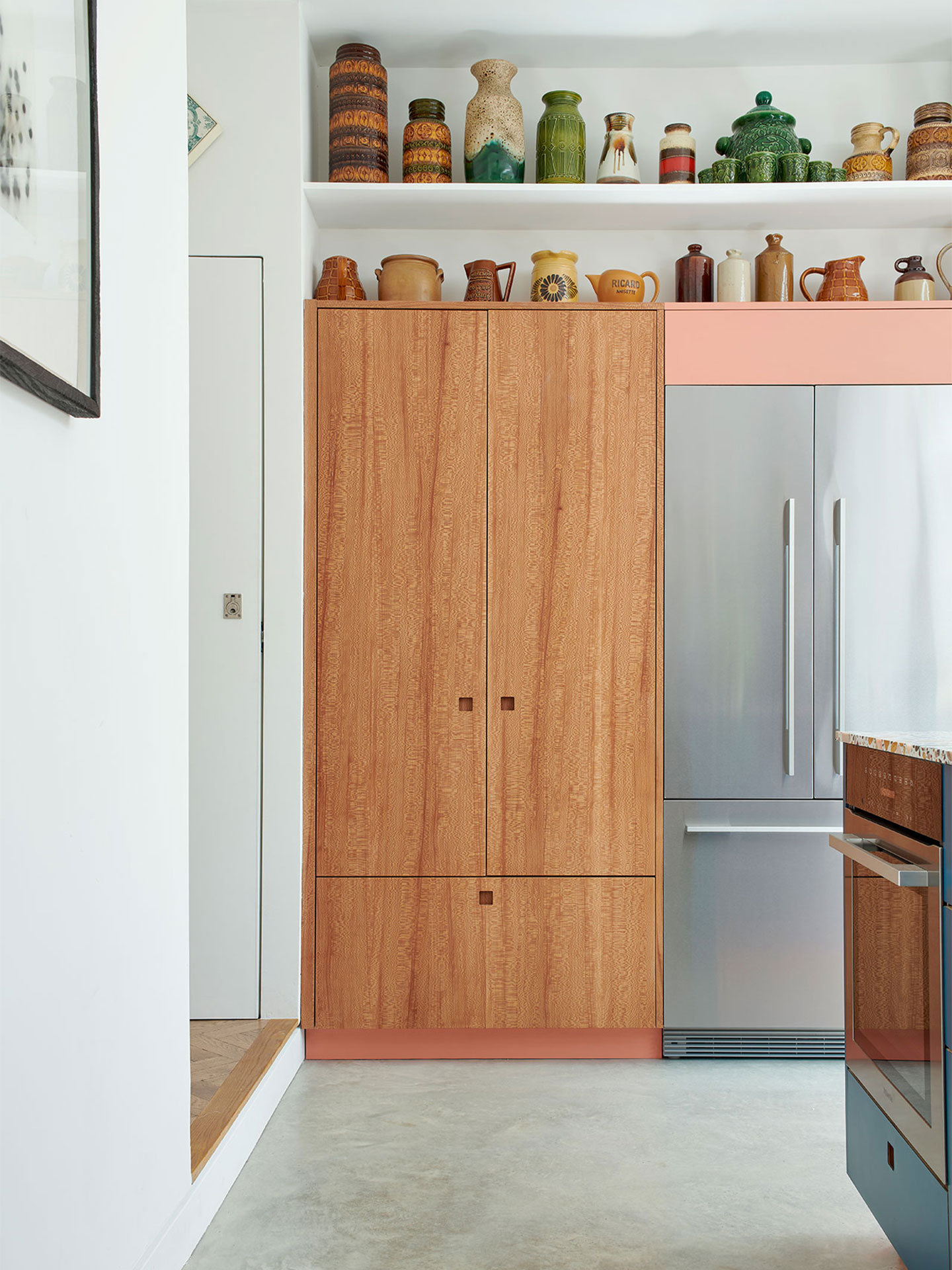 Kitchen including a rich blue, terrazzo topped island, London Plane wood and pink cabinetry.
