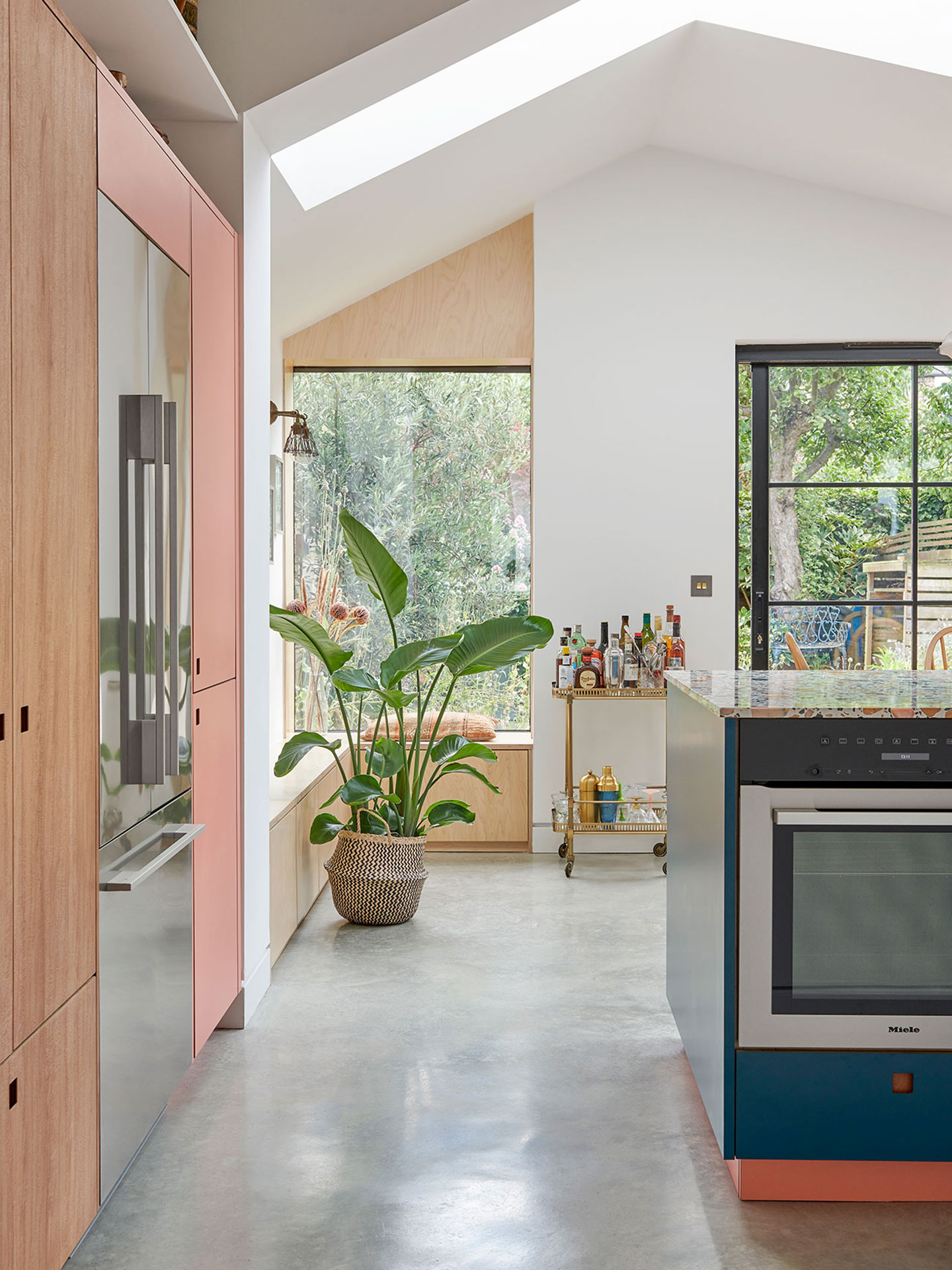 Kitchen including a rich blue, terrazzo topped island, London Plane wood and pink cabinetry.