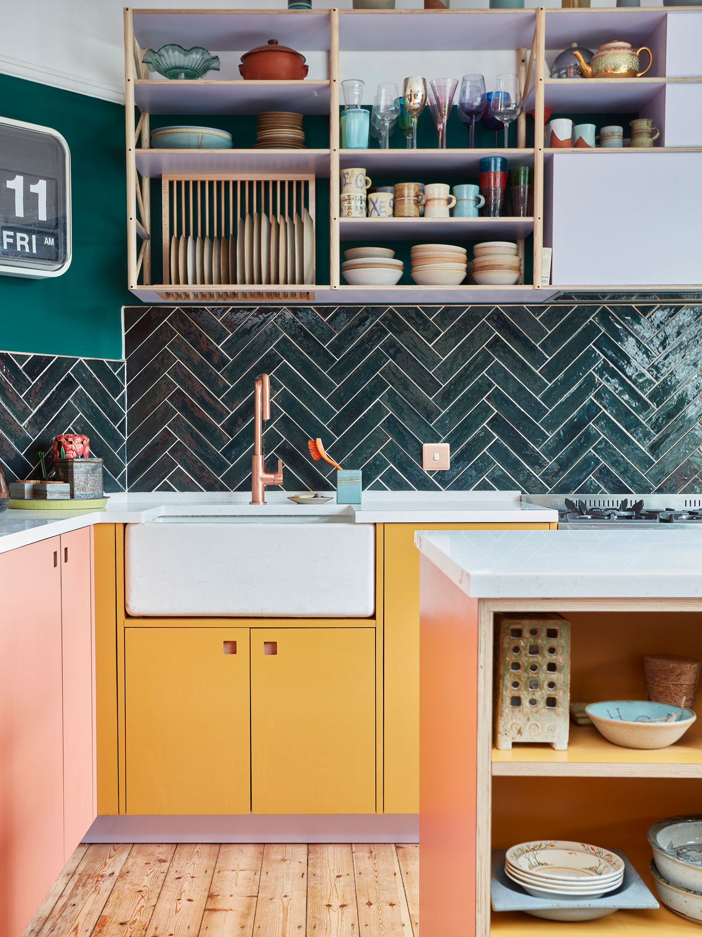 Colourful Pluck kitchen including coral pink, mustard yellow and lilac cabinetry with glossy green tiles and walls.