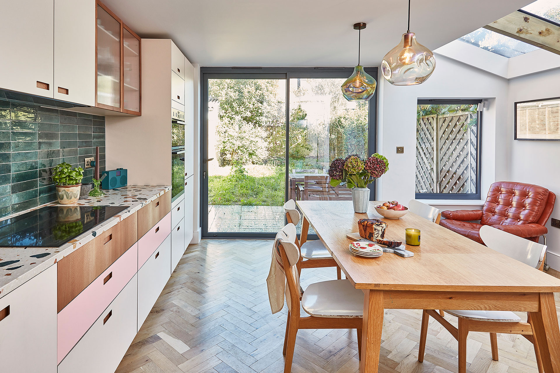 Pink, white and wood kitchen with a green tile splashback and warm wood floor.
