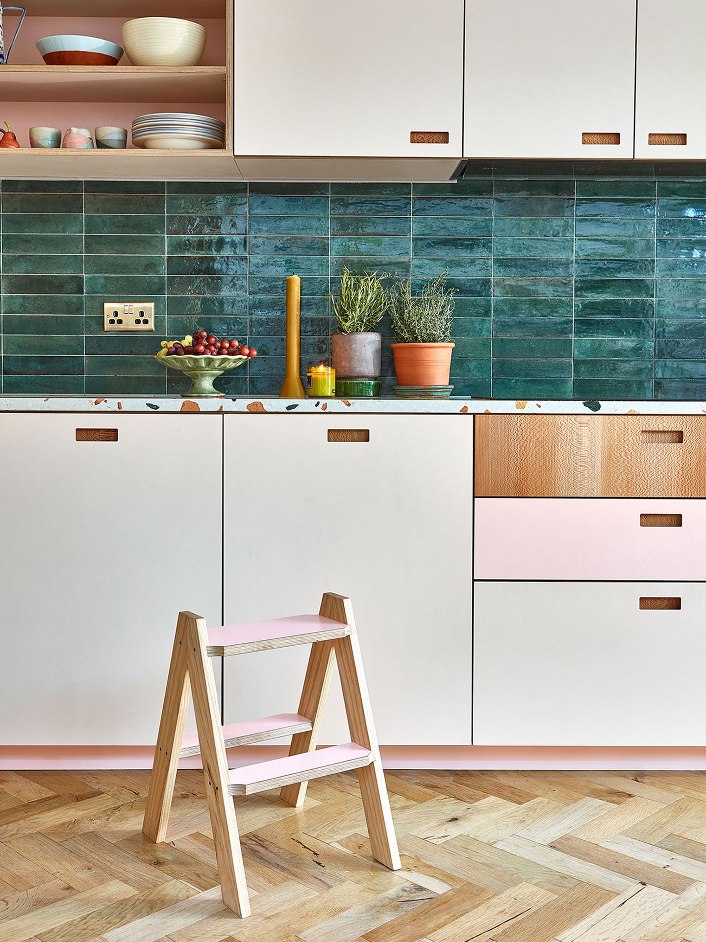 Pink, white and wood kitchen with a green tile splashback and warm wood floor.