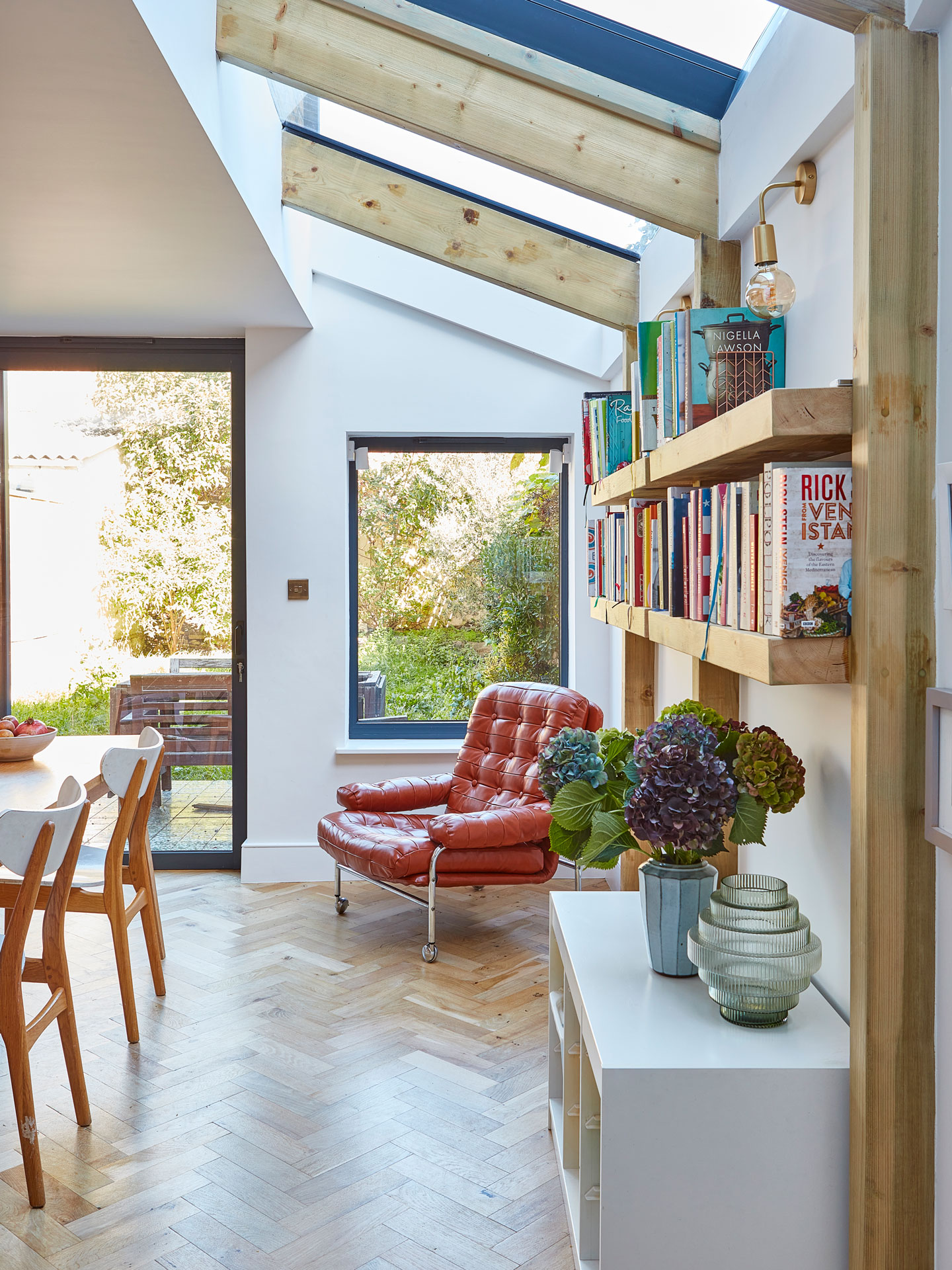 A family home with a pink, white and wood kitchen with a green tile splashback and warm wood floor.