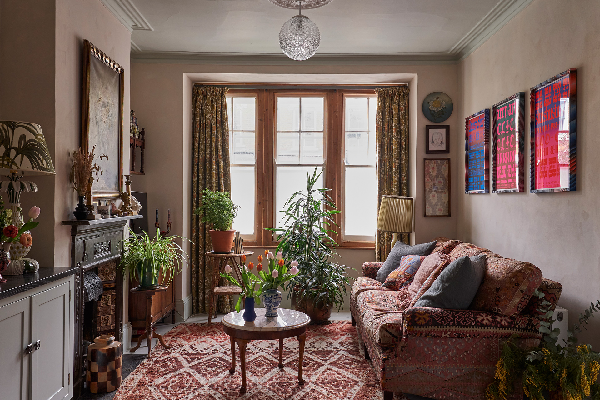 Cosy living room scene with Victorian features, a patterned sofa and moroccan rug are surrounded by houseplants and artwork.
