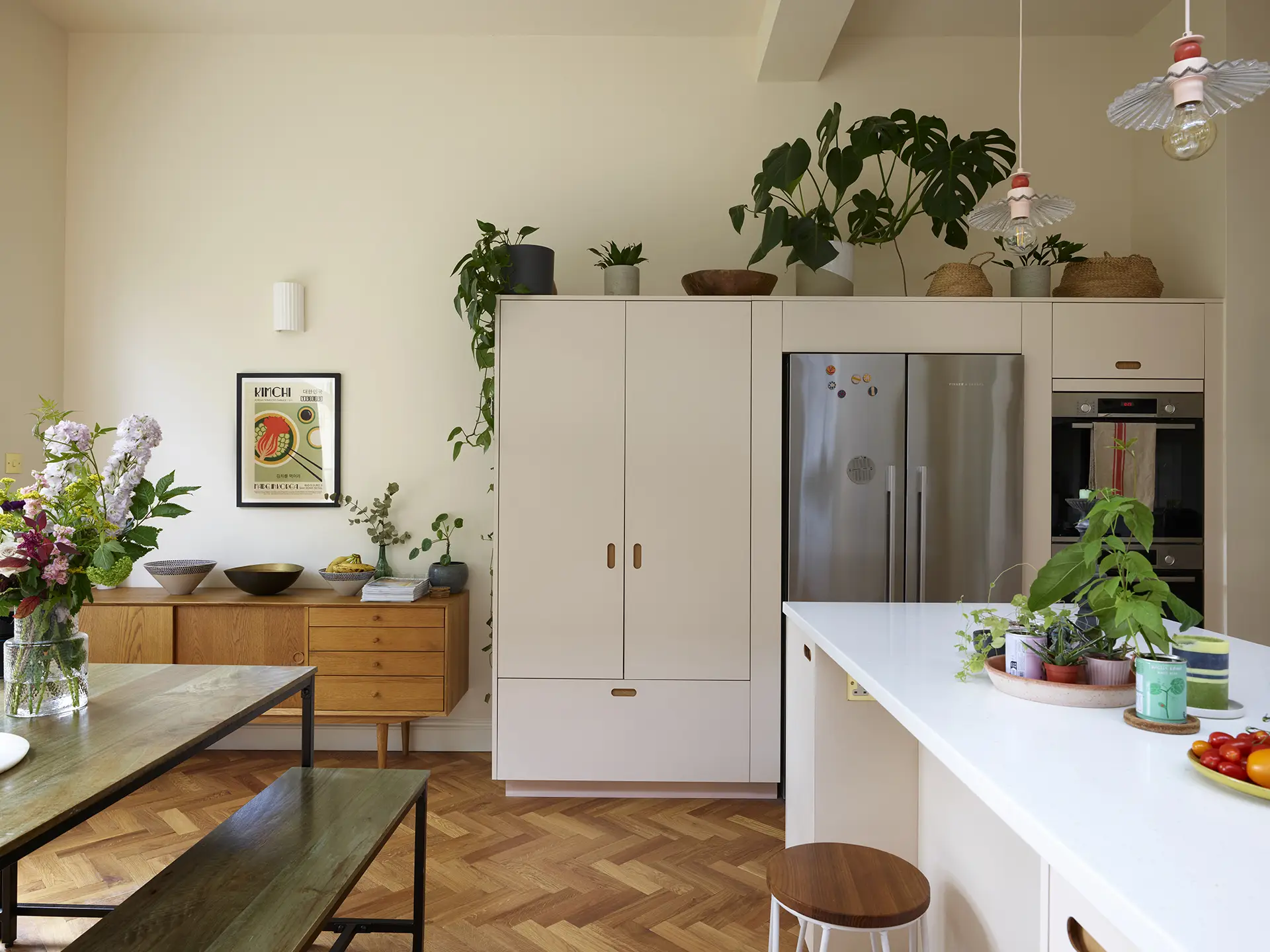 Neutral hues in an open plan family kitchen with a larder, island, dining table and green glazing.