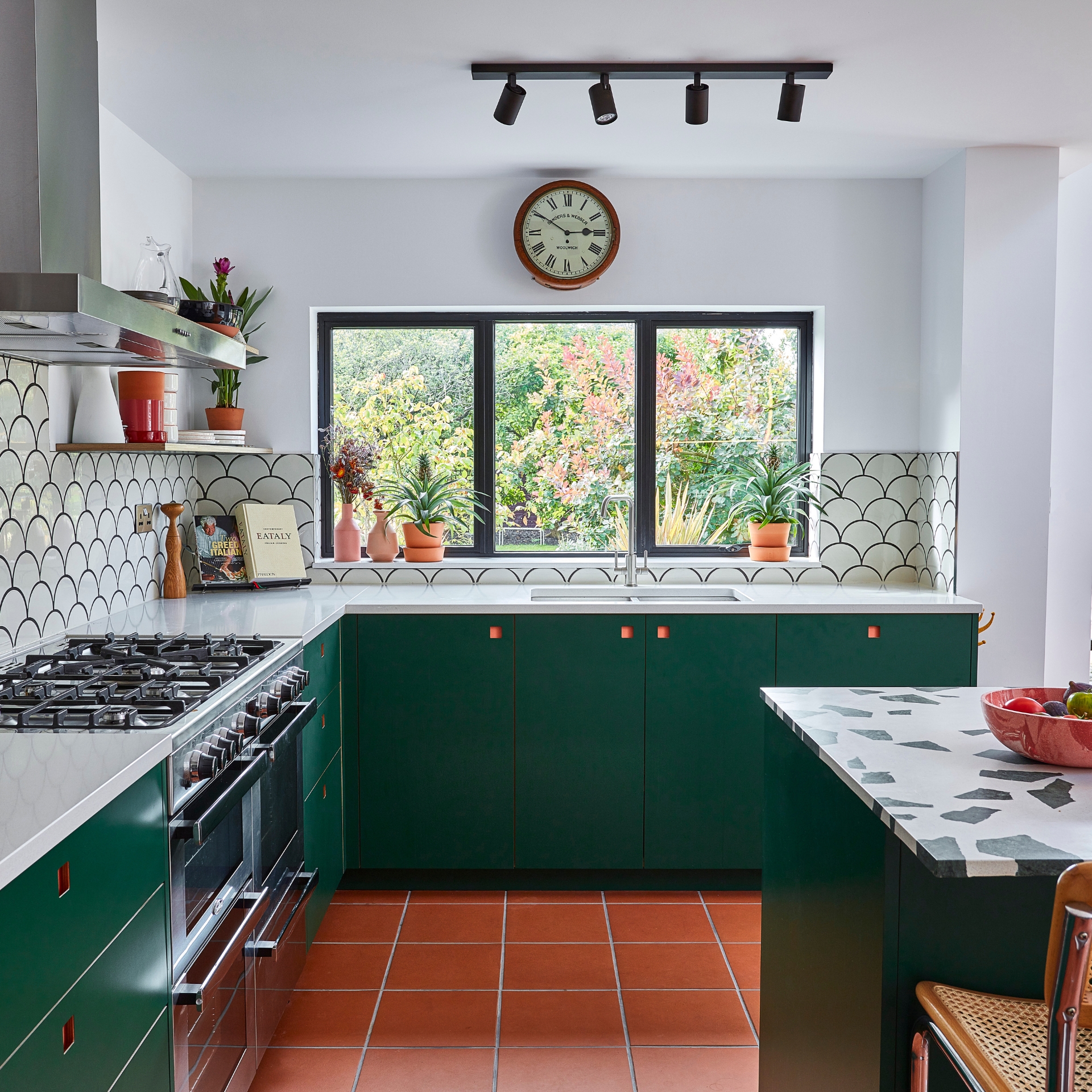Pluck's dark green kitchen cabinetry, terracotta floor tiles and a central island with a bold terrazzo worktop.