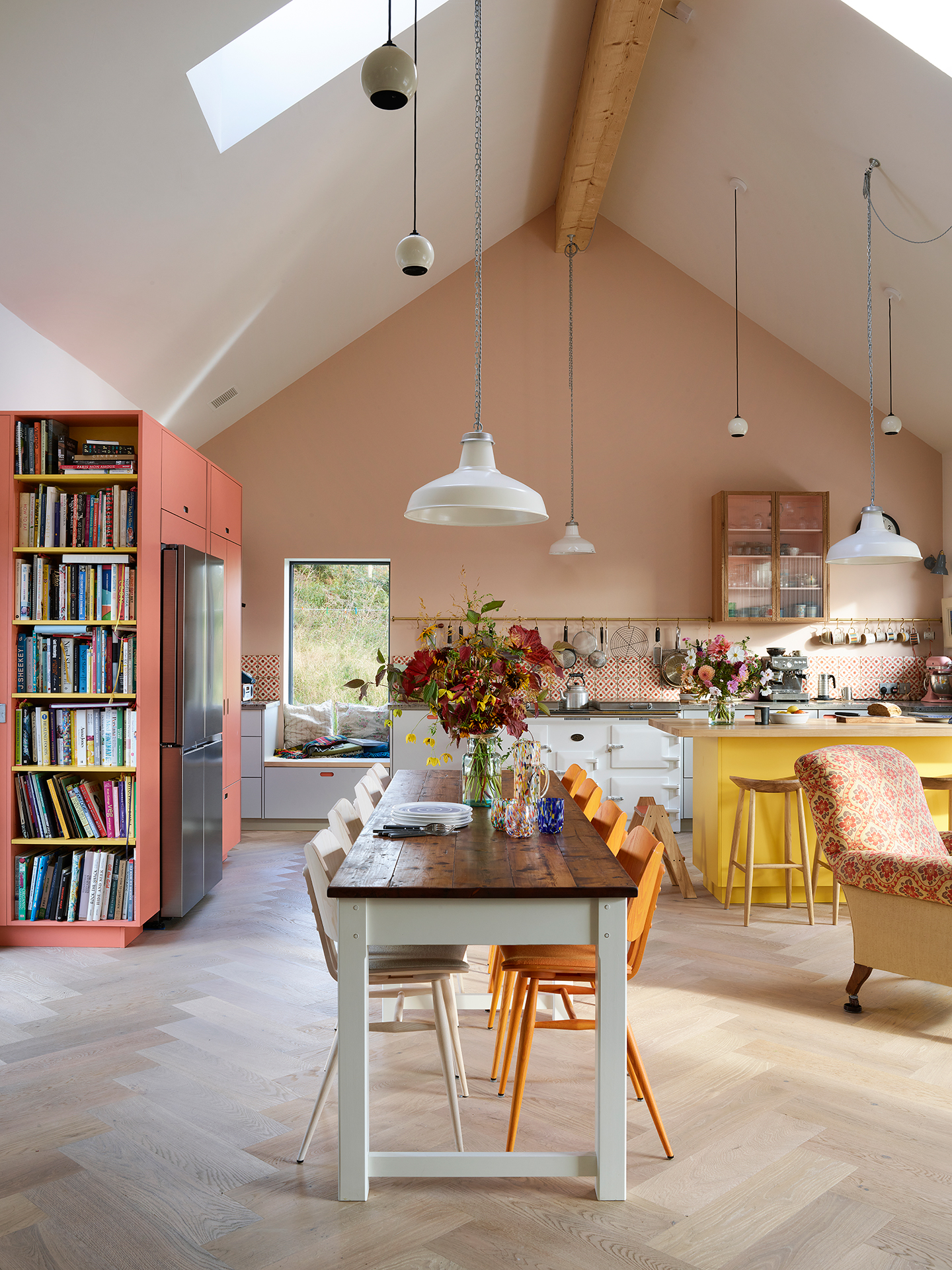 Colourful open plan kitchen in the Scottish Highlands including a peninsula with a wooden worktop, shelving, glass cabinet and Pluck utility.