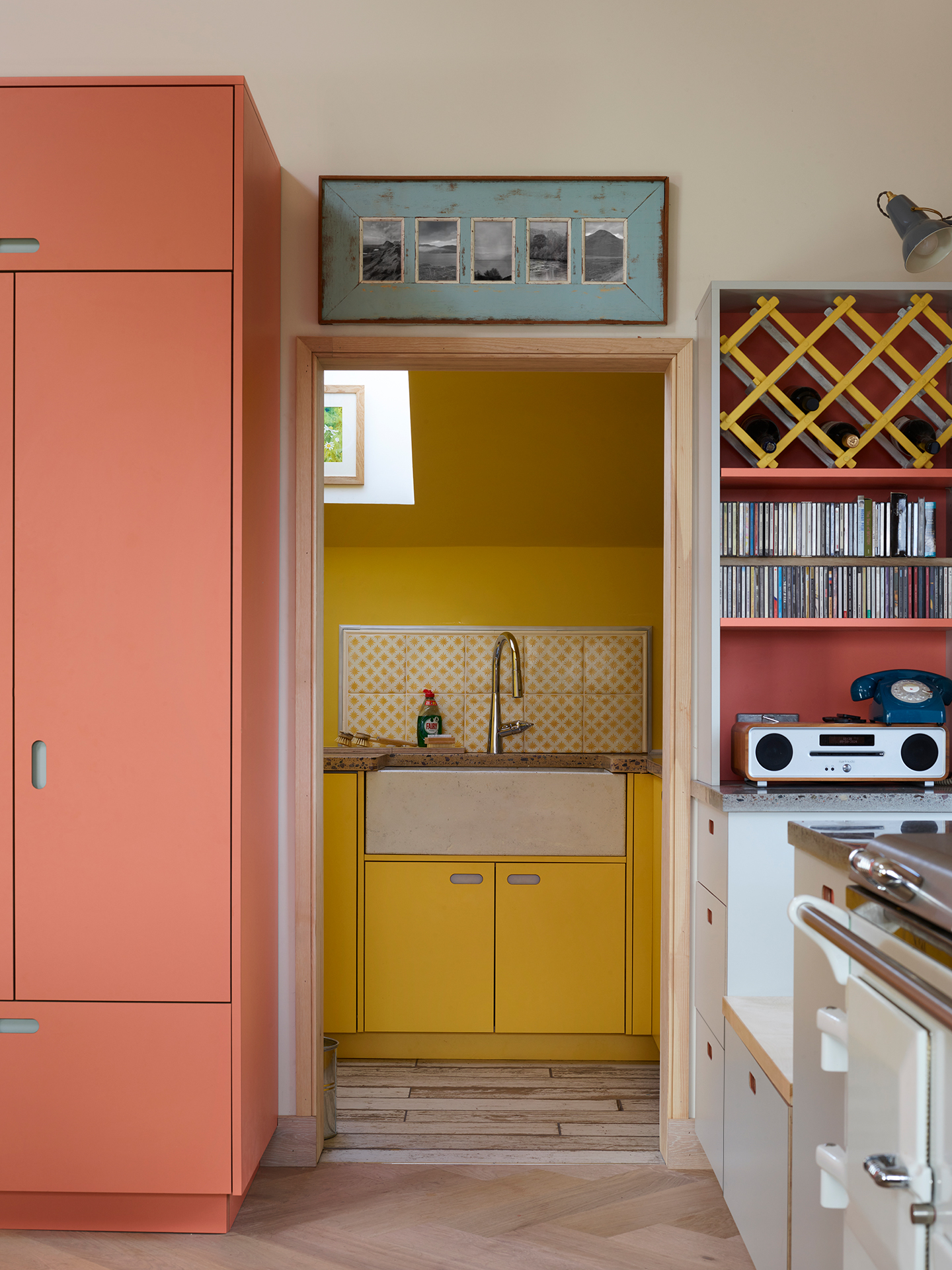 Colourful open plan kitchen in the Scottish Highlands including a peninsula with a wooden worktop, shelving, glass cabinet and Pluck utility.