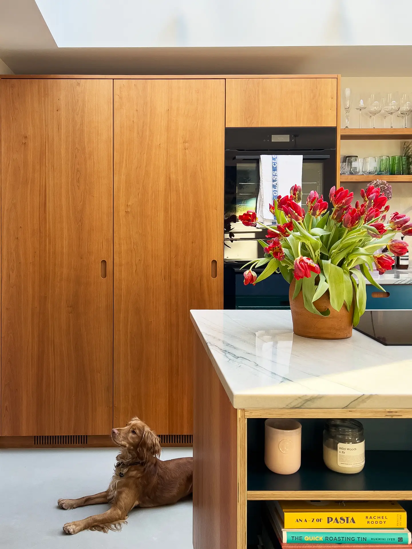 Pluck kitchen with cherry wood cabinets, a marble topped island and a vase of red tulips.