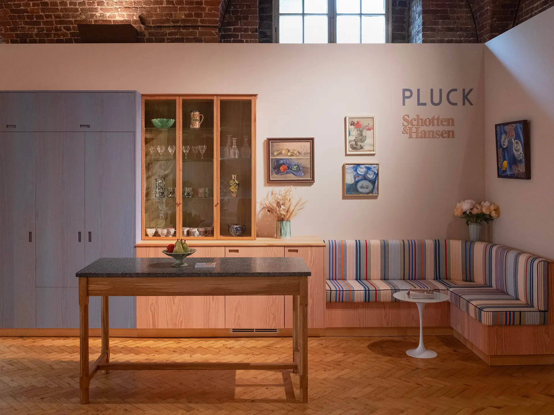 Pluck kitchen with blue and pink coloured wood cupboards plus a tall glass cabinet displaying ceramics.