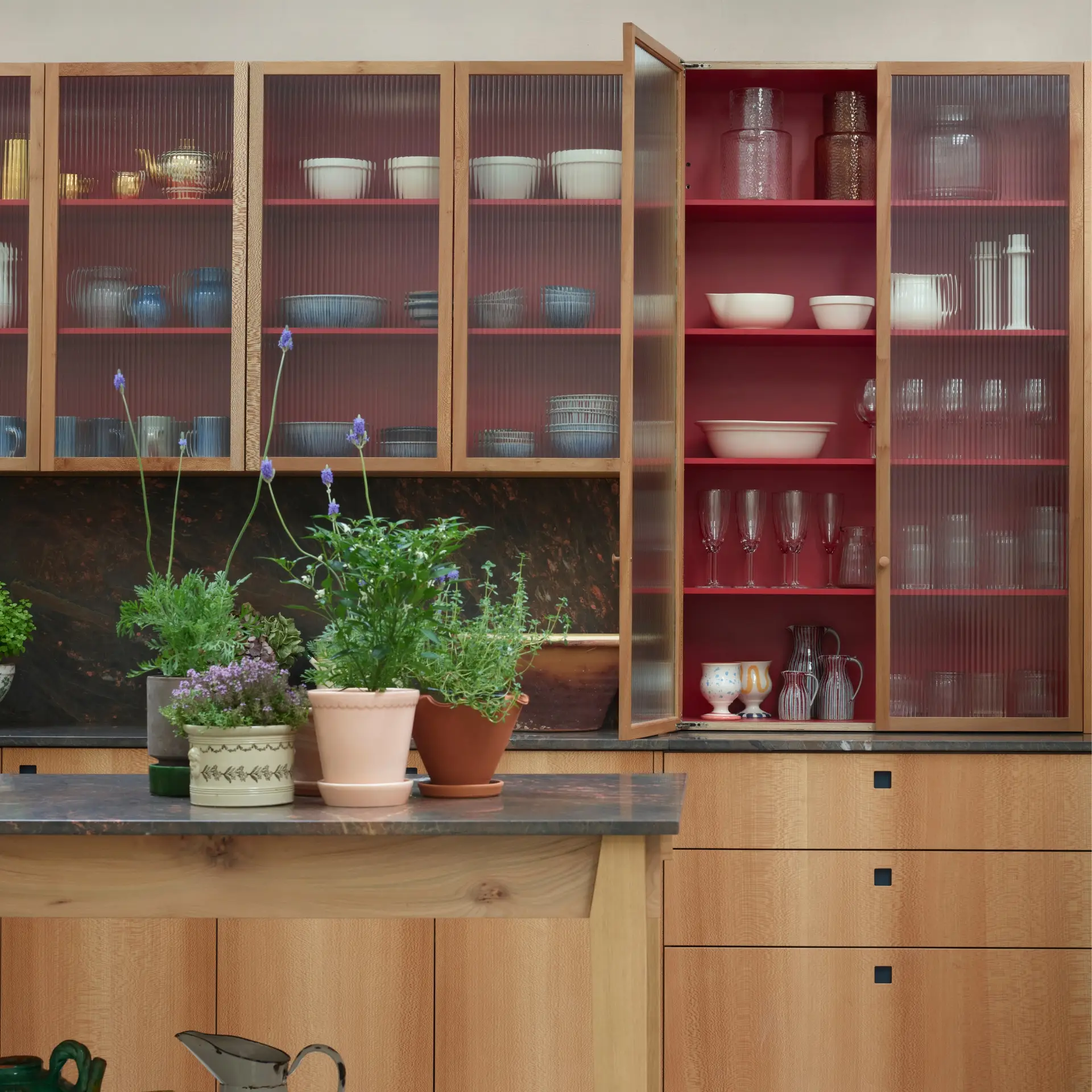 Kitchen showroom with London Plane, rich red and deep blue cupboards and a wooden work table with quartzite.