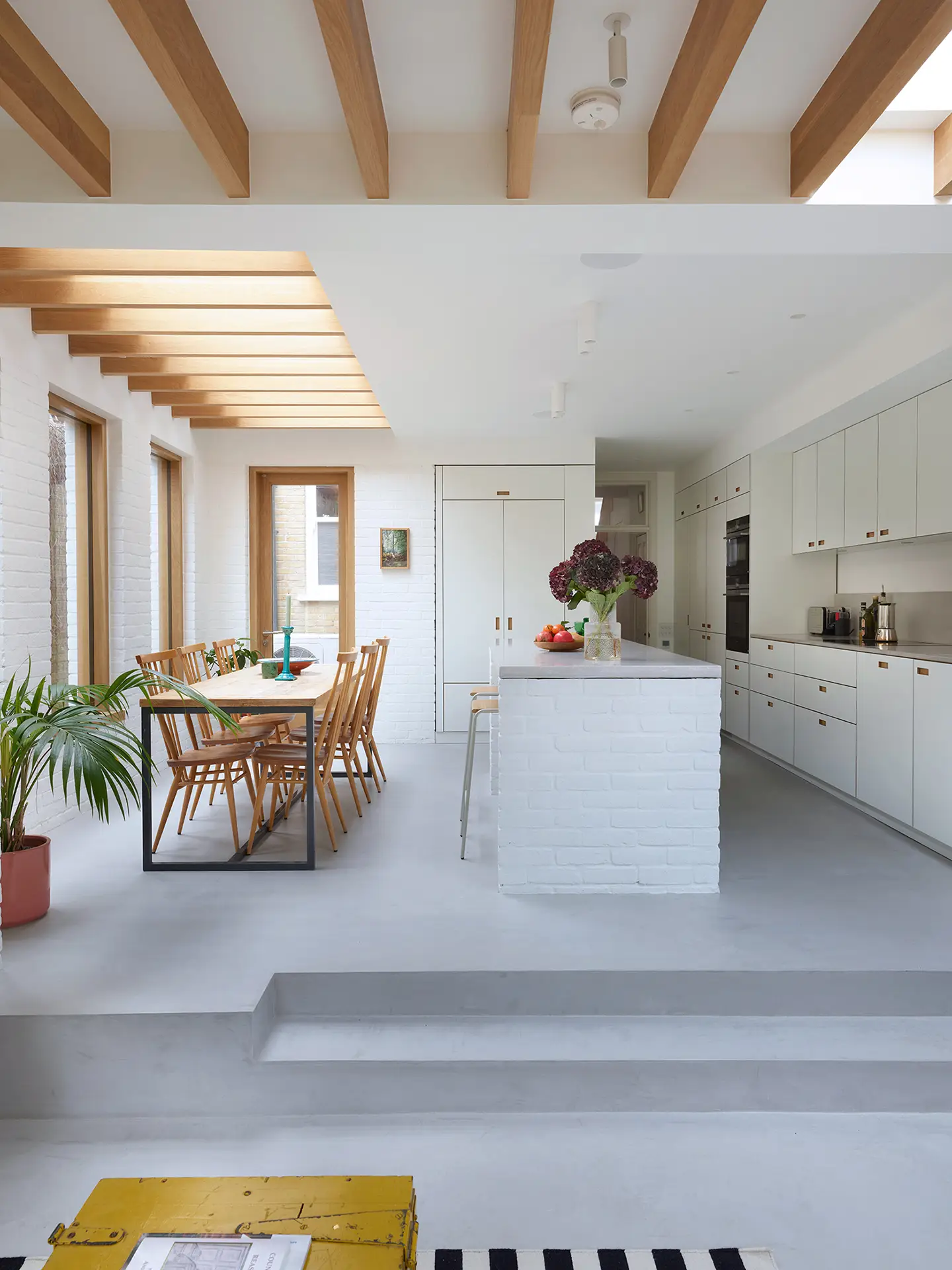 Minimalist kitchen in a wraparound extension, home to an architect and including white Pluck cabinetry with warm wood handles.
