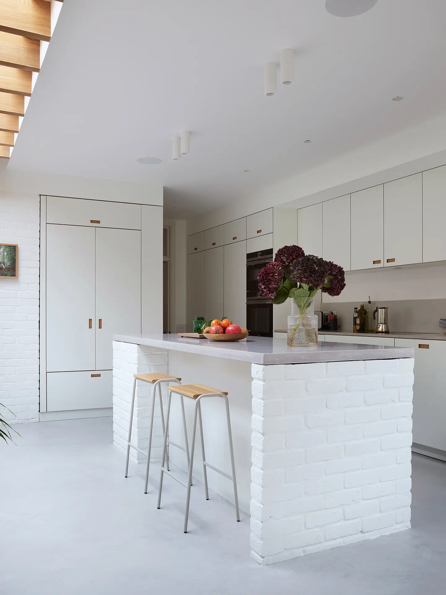 White kitchen in an open plan space with wood beams and exposed painted bricks.