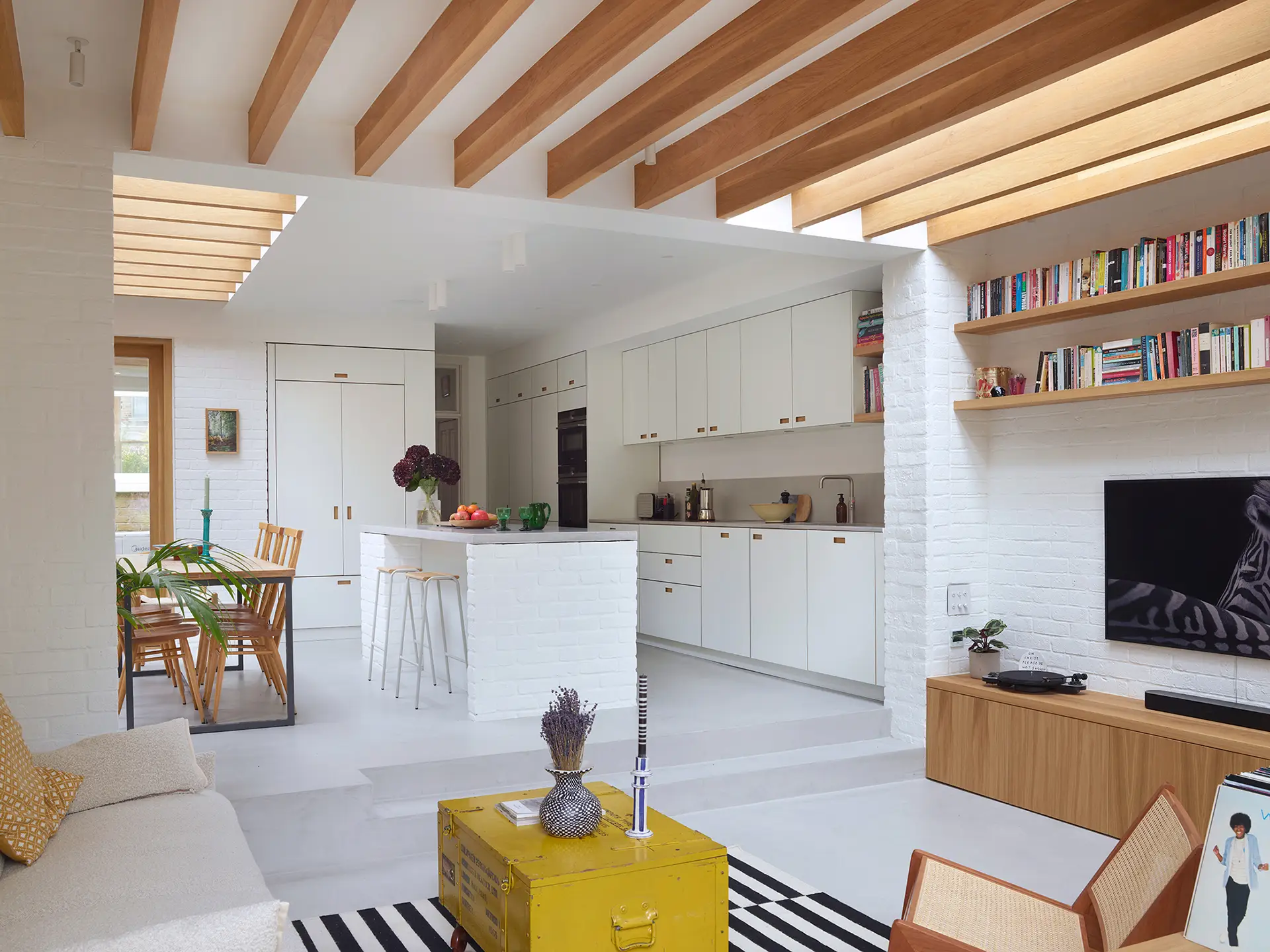 Minimalist kitchen in a wraparound extension, home to an architect and including white Pluck cabinetry with warm wood handles.