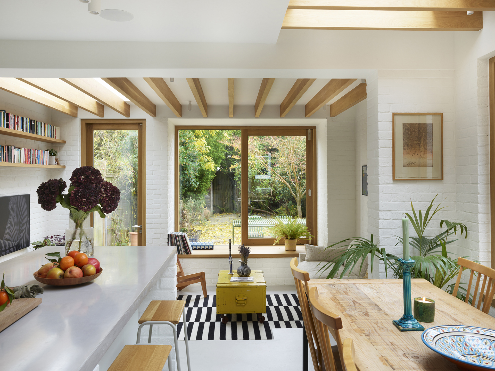 Minimalist kitchen in a wraparound extension, home to an architect and including white Pluck cabinetry with warm wood handles.